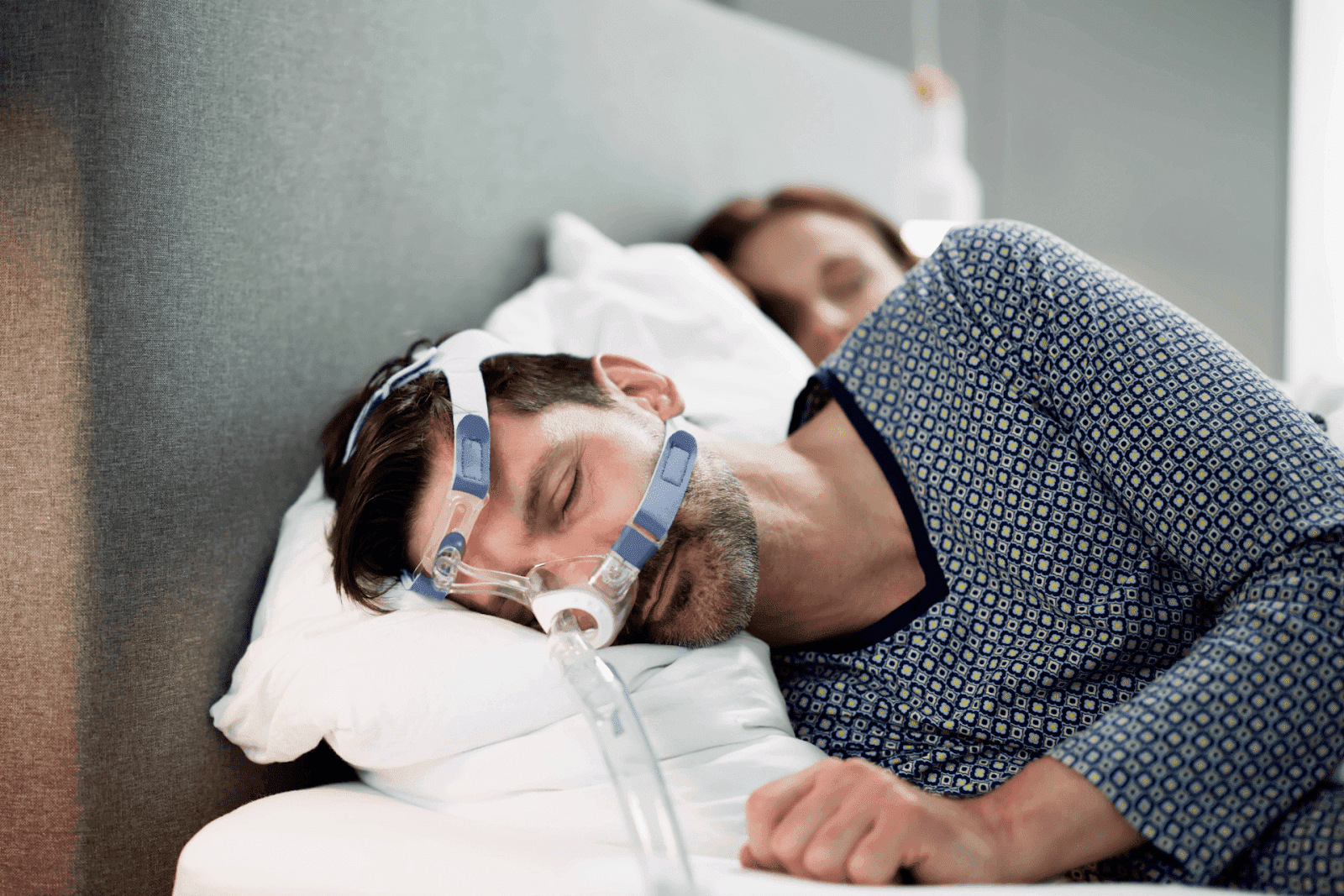 Man sleeping with a CPAP mask on for sleep apnea treatment, lying beside his partner in bed.