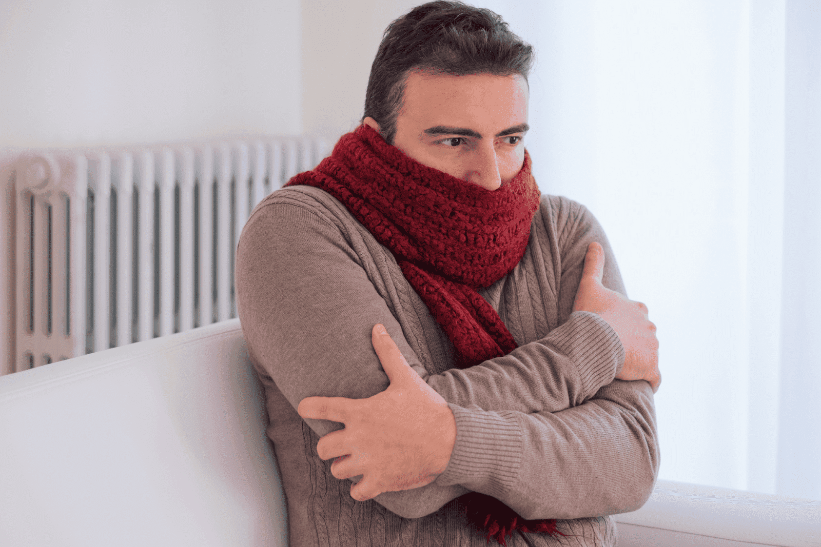Man wearing a red scarf shivering indoors, hugging himself for warmth
