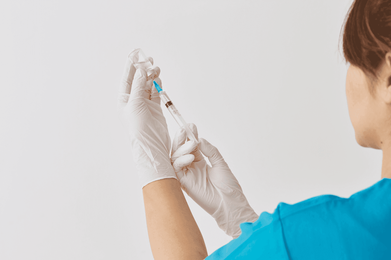 Medical professional drawing liquid from a vial with a syringe