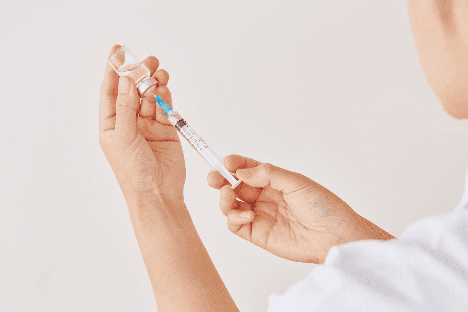 Medical professional drawing liquid from a vial with a syringe