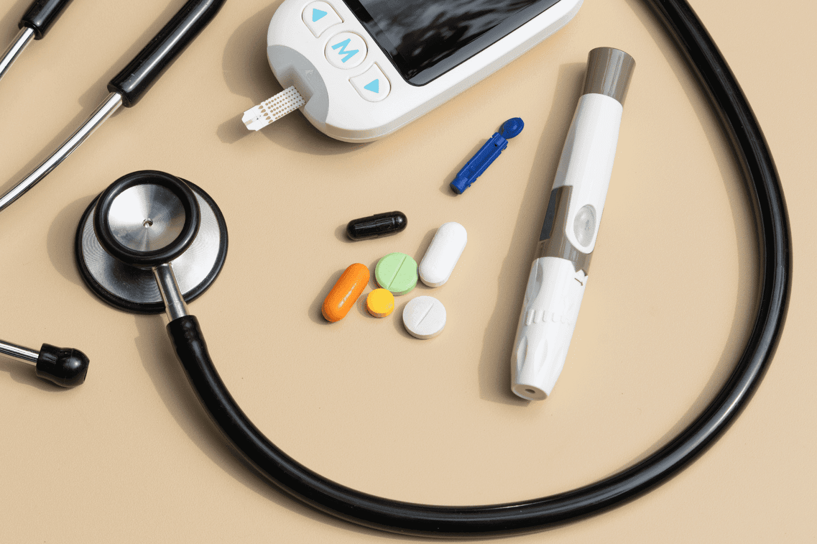 Medical tools and pills with a stethoscope, glucose meter, and lancet on a beige surface