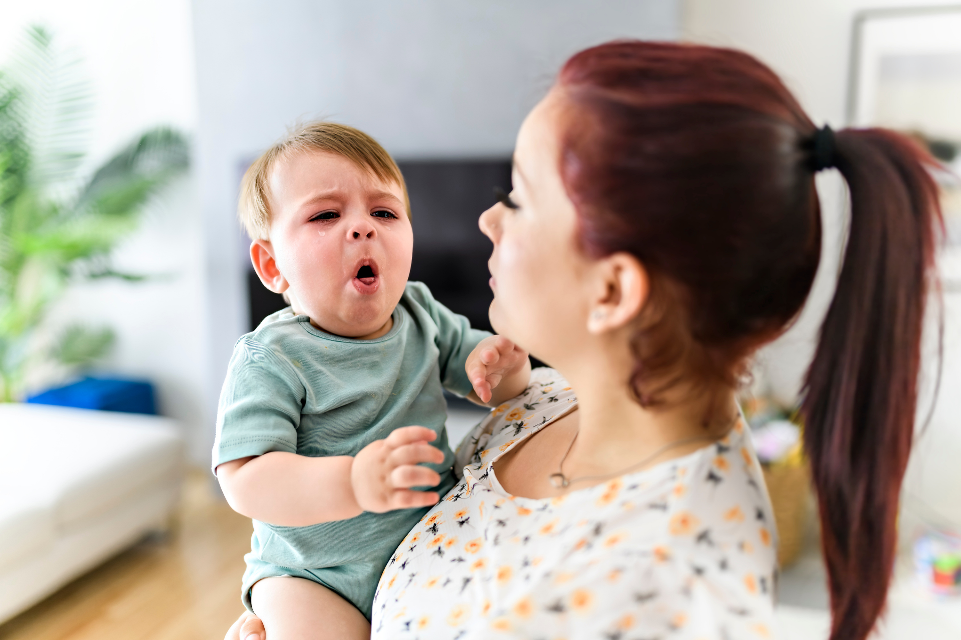 Mother holding a crying baby indoors, appearing concerned