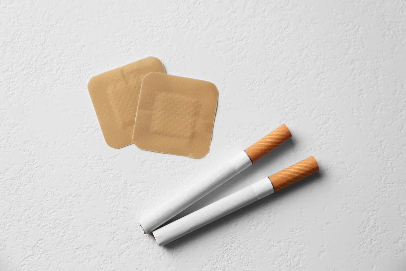 Nicotine patches placed beside two cigarettes on a white surface