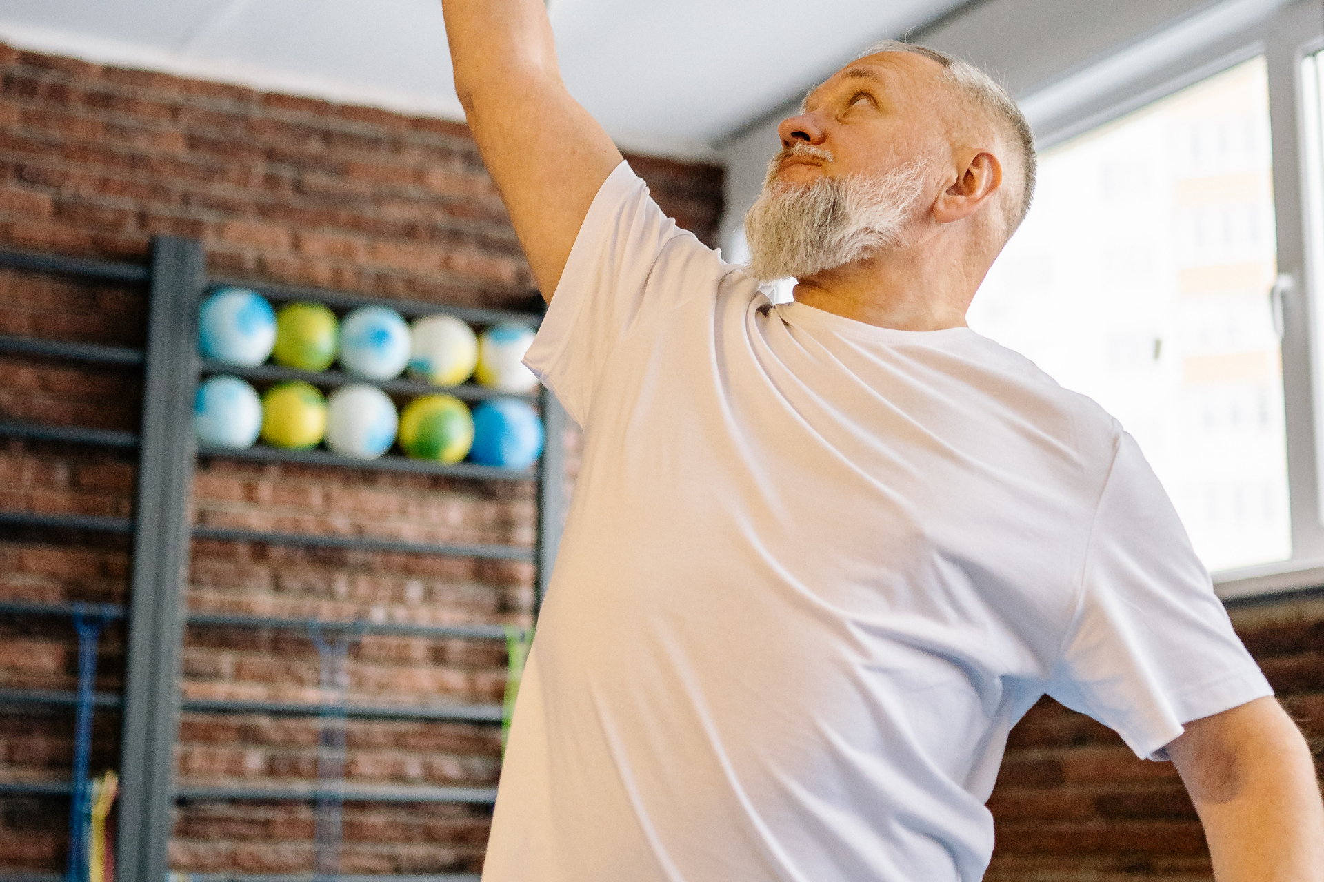Older man stretching with arm raised in a gym