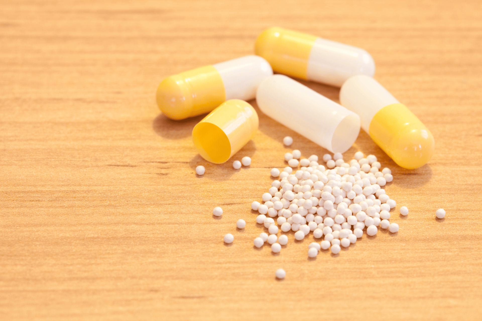Opened yellow-and-white capsules with small white medicine beads spilled on a wooden surface.