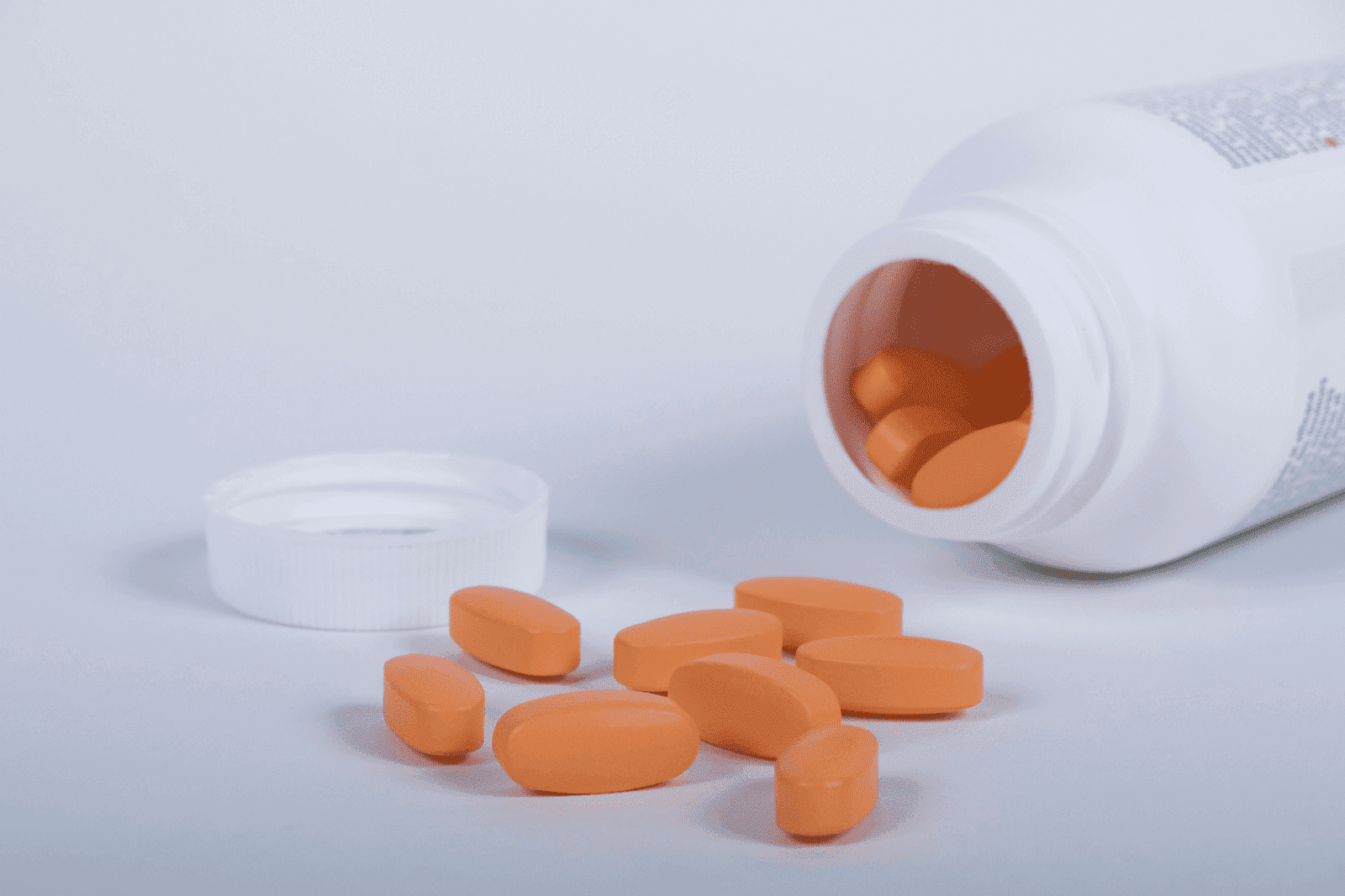 Orange tablets spilled from an open white pill bottle onto a light surface.