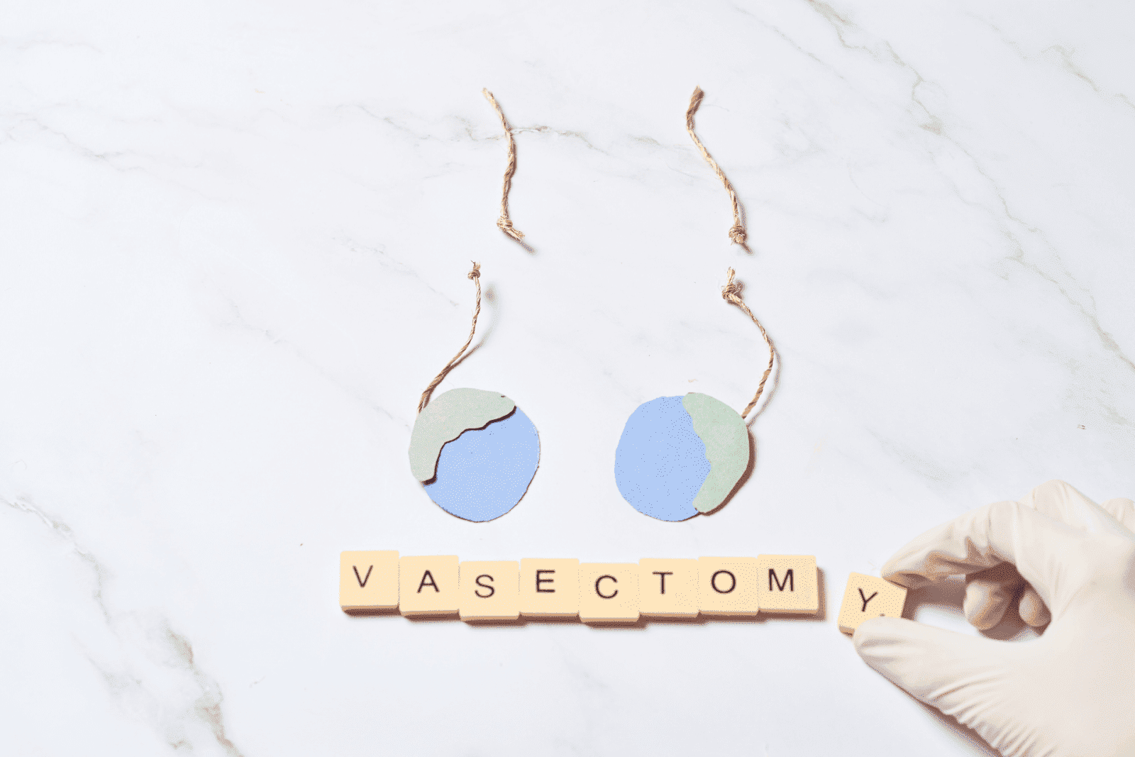 Paper cutout of male reproductive organs above the word “Vasectomy” spelled out in tiles, with a gloved hand placing the letter "Y".