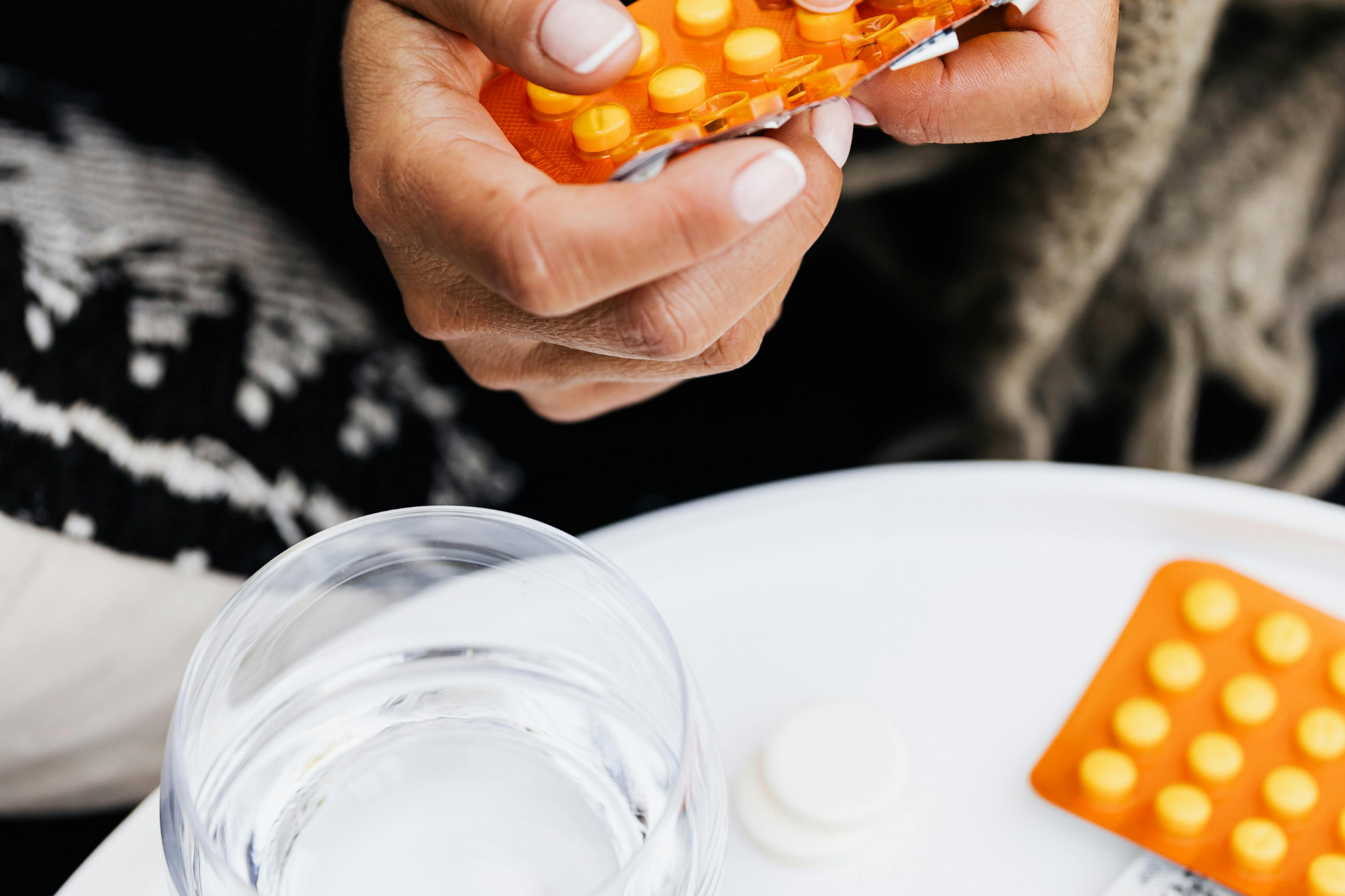 Person holding a blister pack of orange tablets next to a glass of water