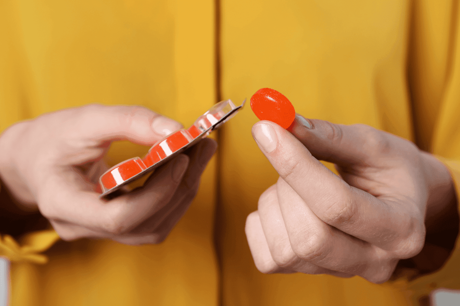 Person holding a red throat lozenge and blister pack.