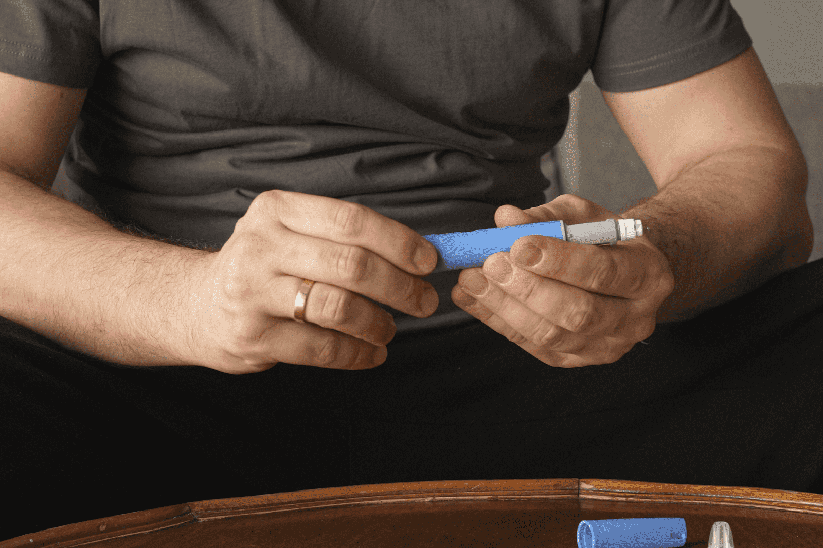 Person holding an insulin pen while preparing for an injection, sitting at a table with diabetes supplies.
