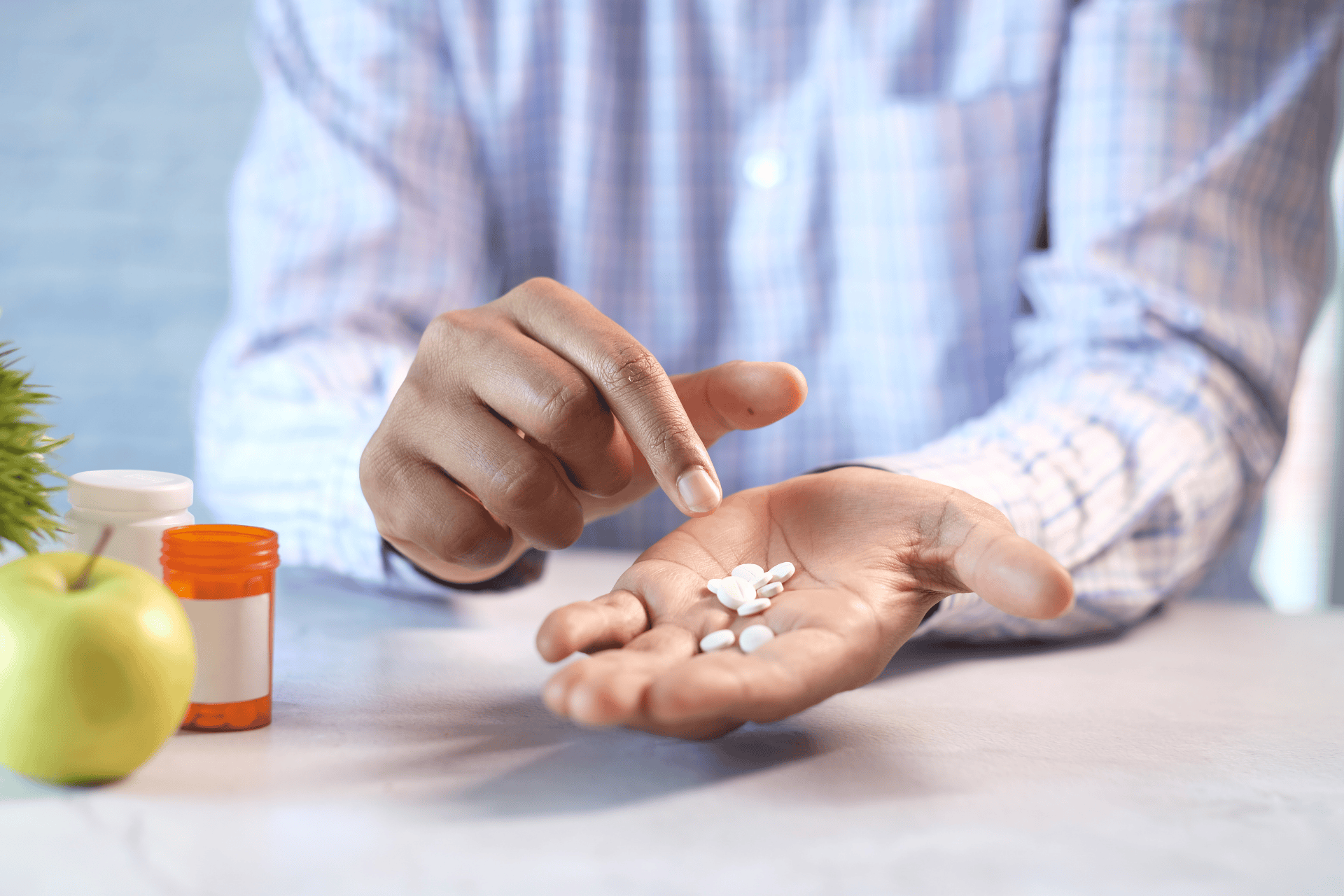 Person holding pills in hand with medicine bottle and apple on the table