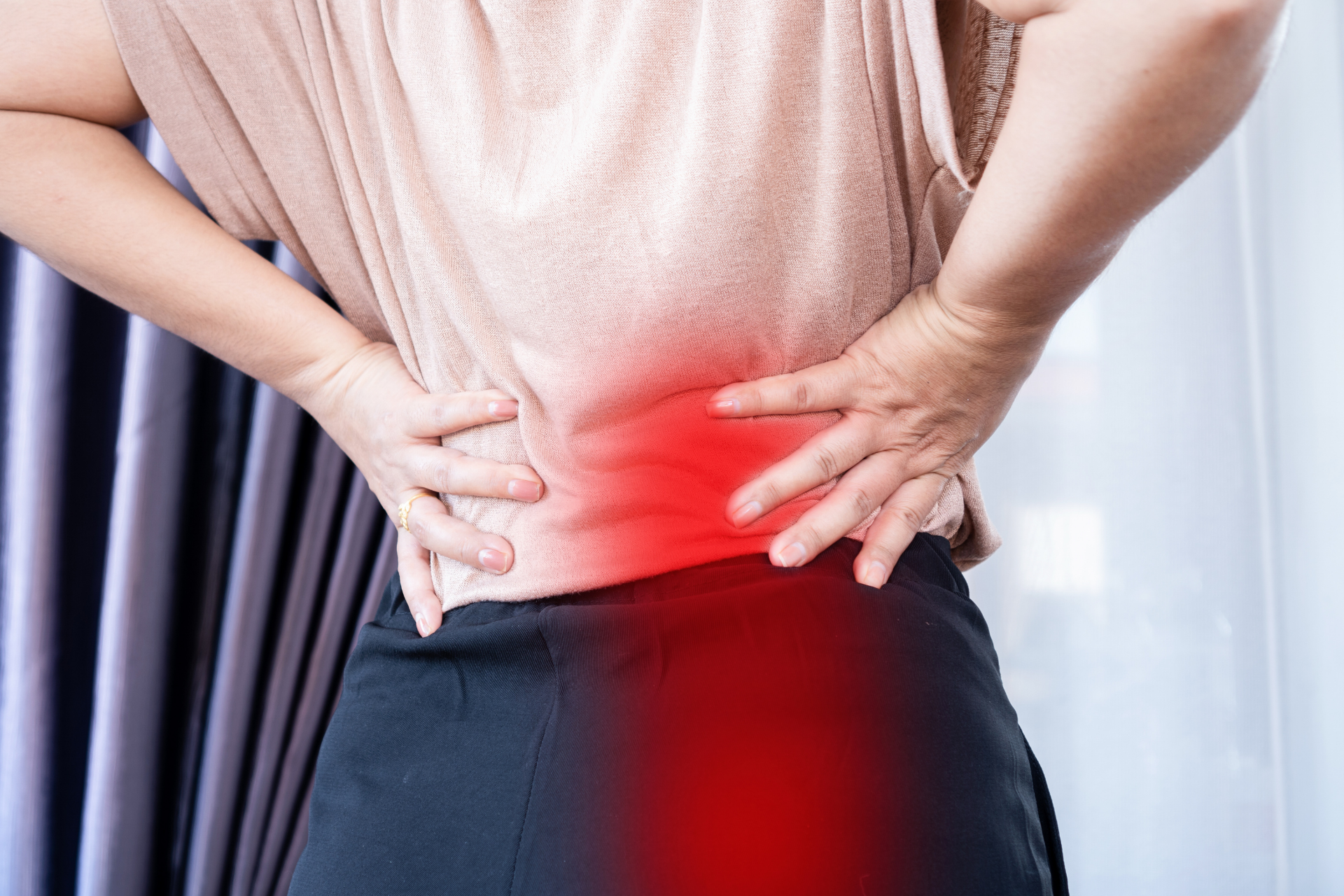 Person holding their lower back with highlighted red area indicating pain