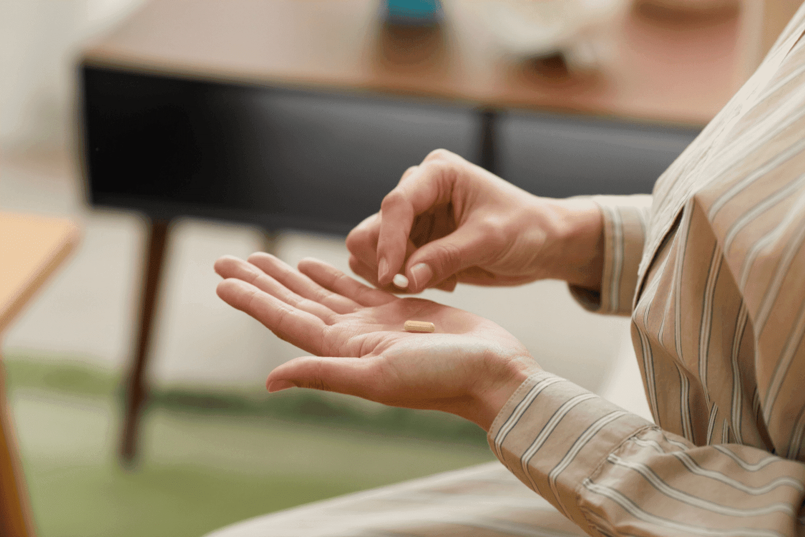 Person holding two pills, one white and one yellow capsule, in their hand