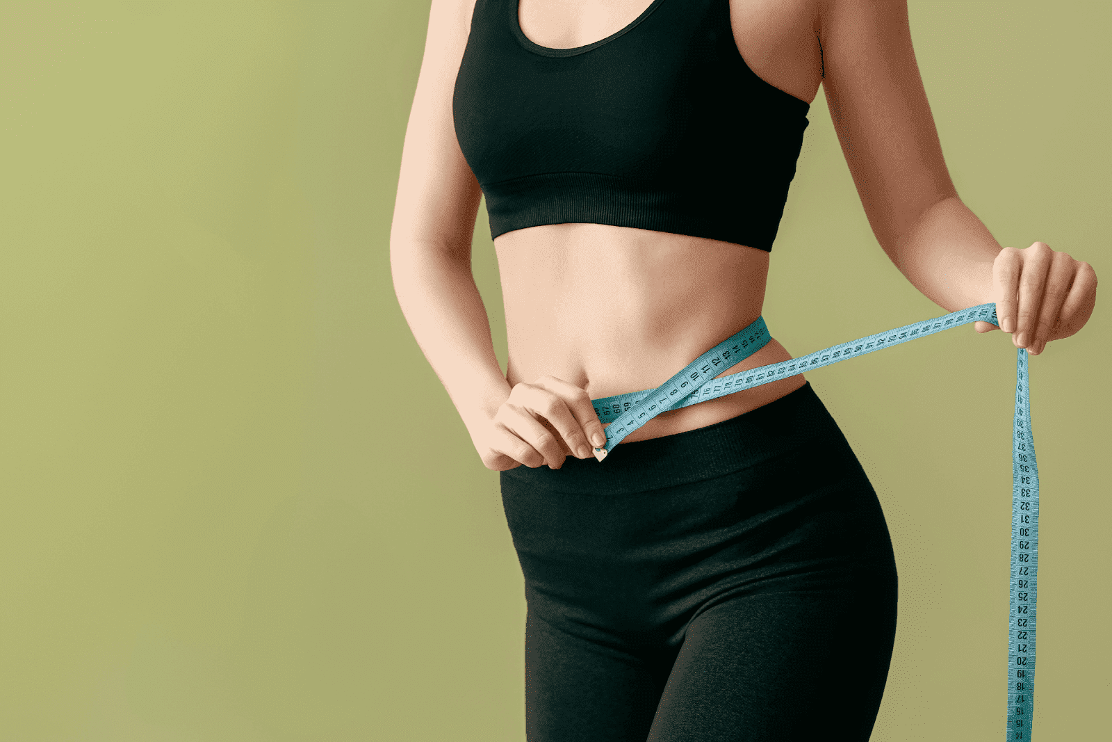 Person in fitness clothing measuring their waist with a tape measure