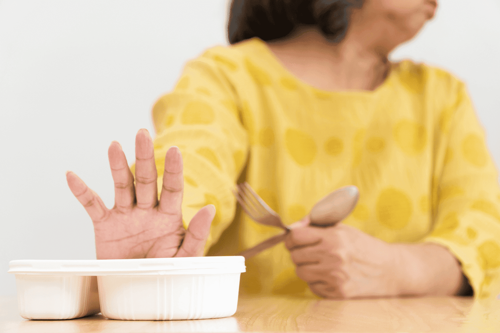 Person in yellow shirt pushing food away