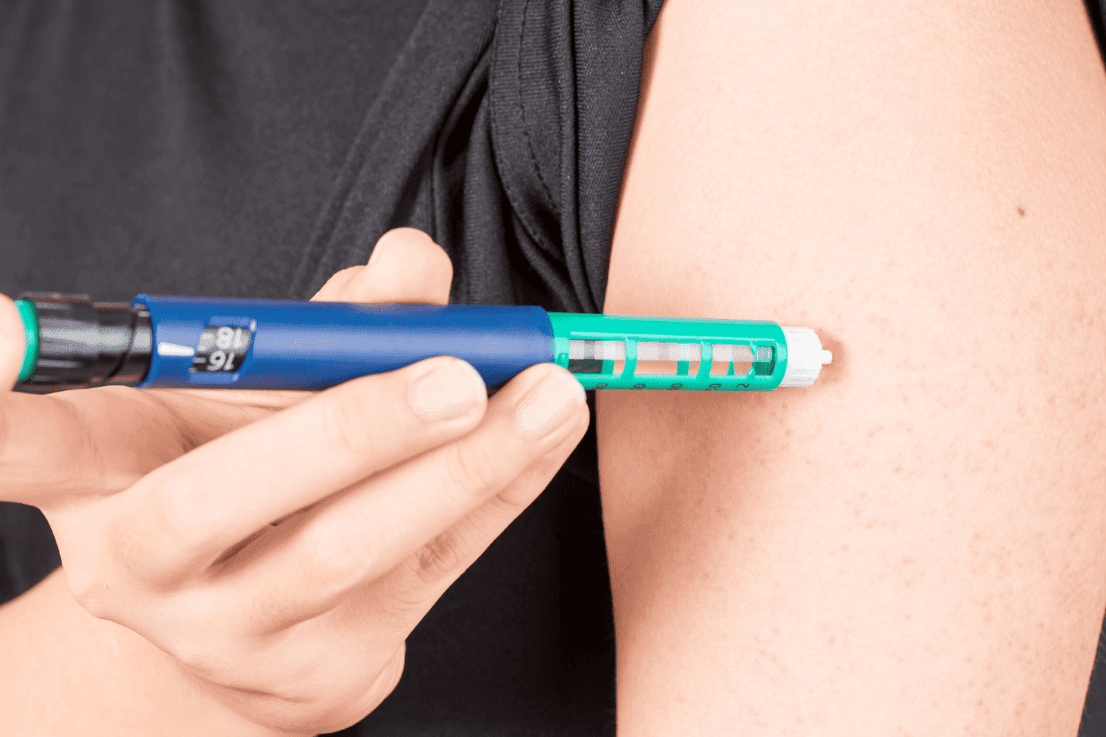 Person injecting medication into their upper arm using a blue and green insulin pen