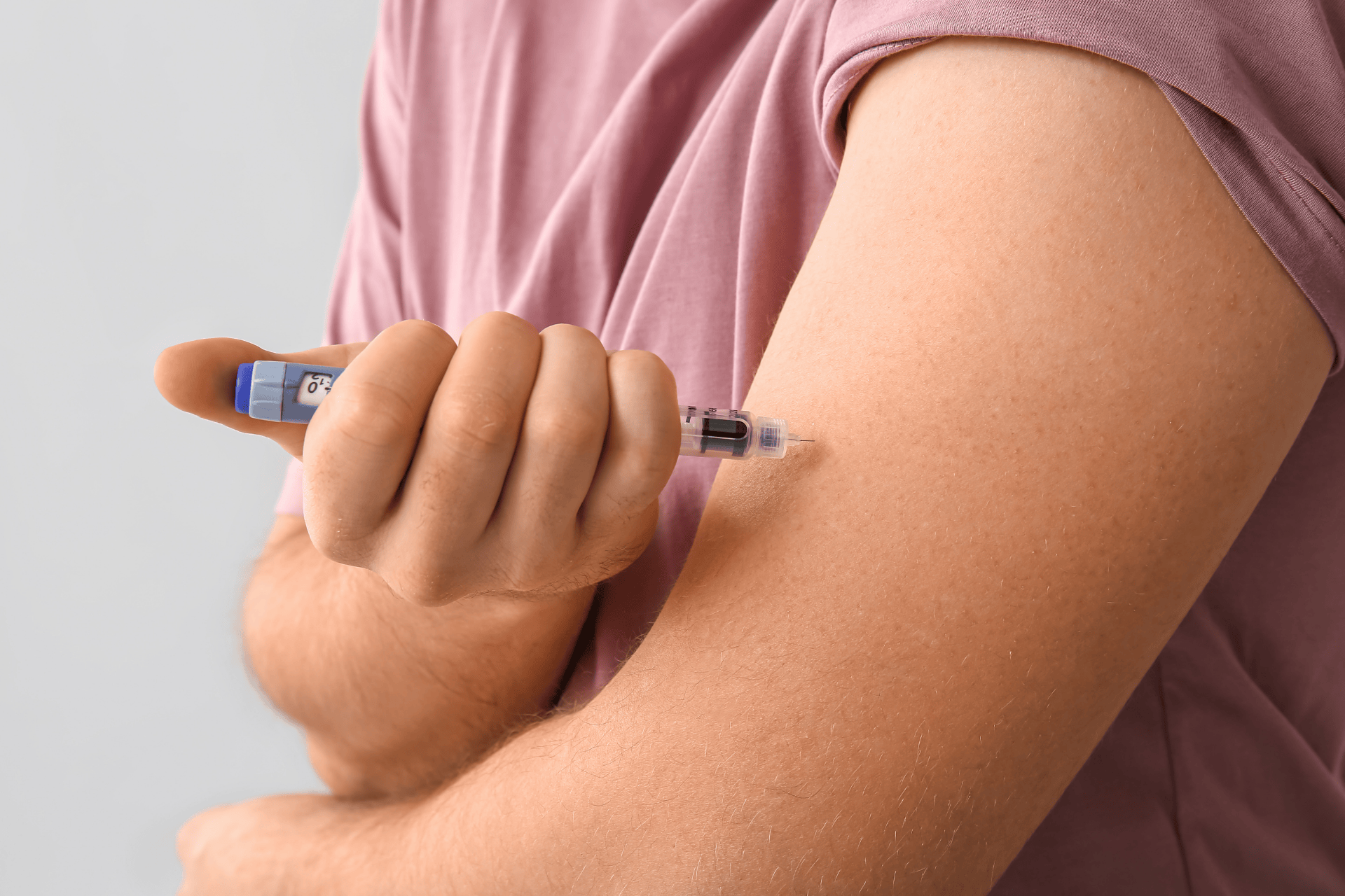 Person injecting their upper arm with an insulin pen.