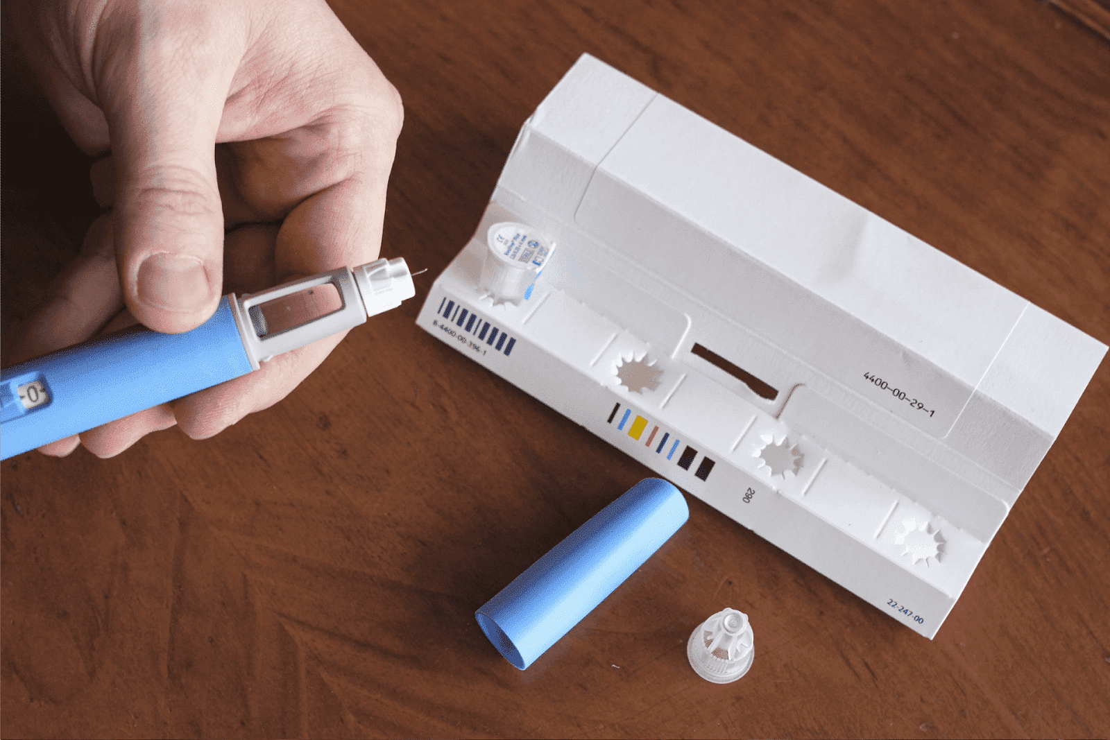 Person preparing an insulin pen with medication and packaging on a wooden table
