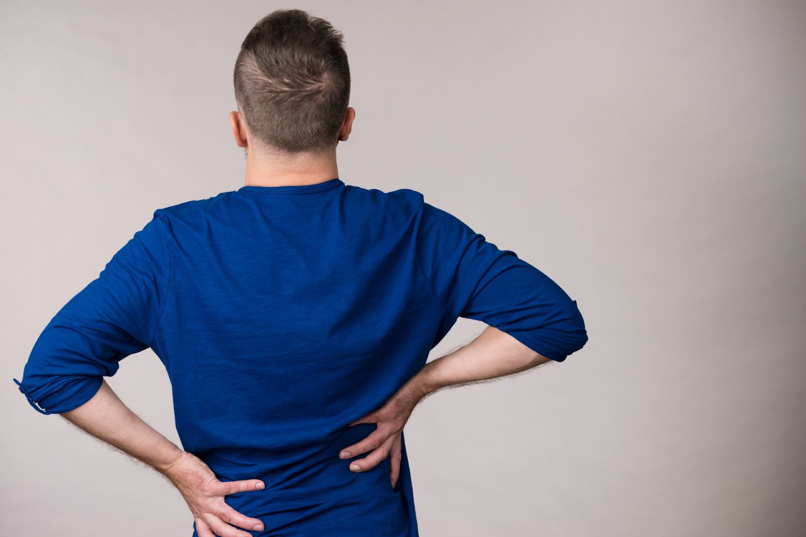 Person seen from behind holding their lower back with both hands, suggesting back pain or discomfort