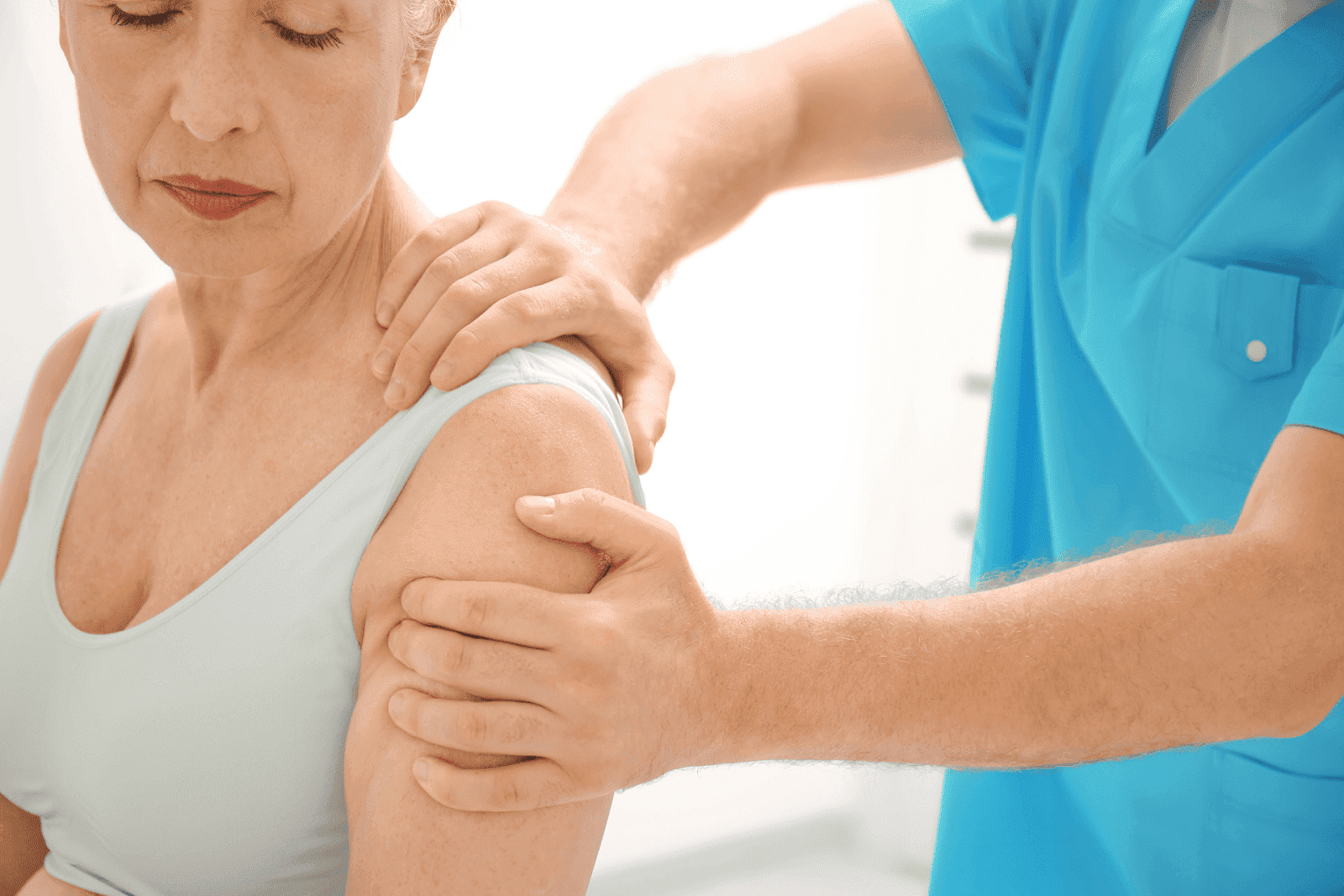 Physiotherapist examining elderly woman's shoulder.