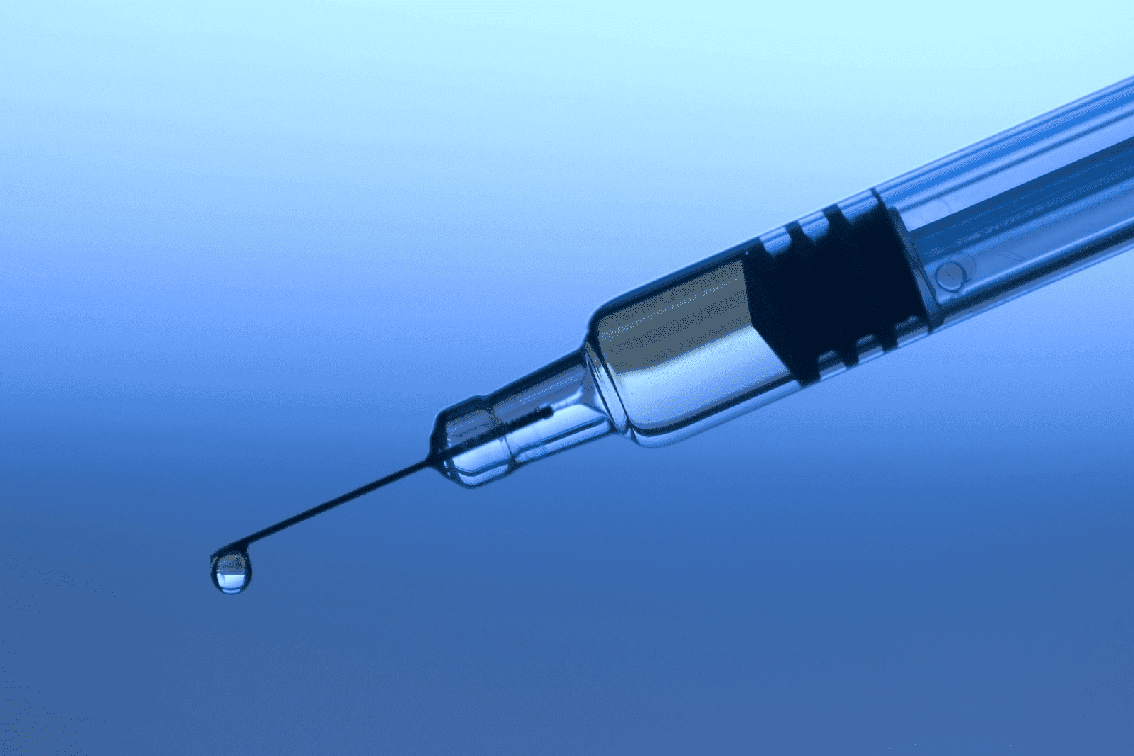Close-up of a syringe needle with a droplet of liquid against a blue background