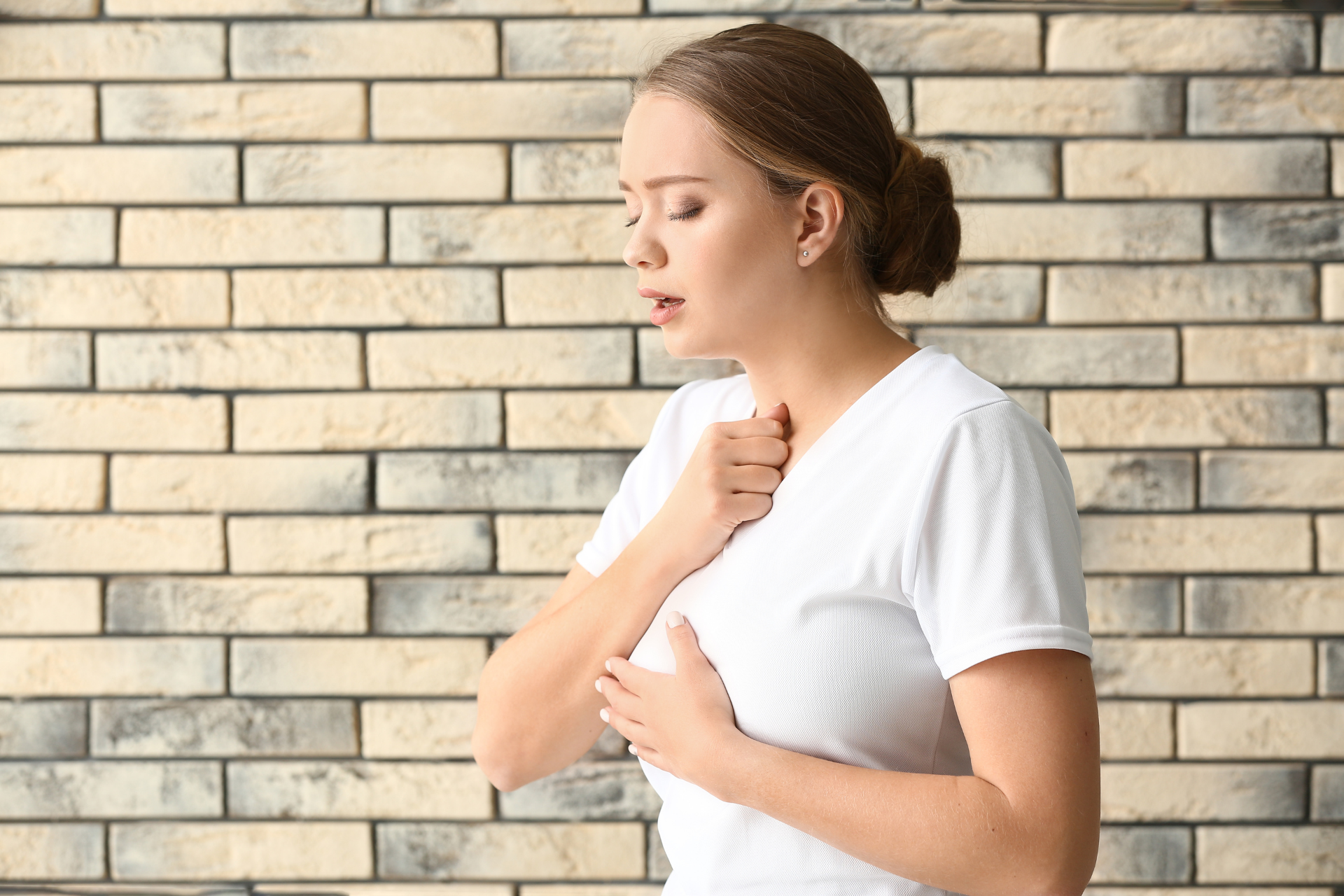 A woman clutching her chest and throat with her eyes closed, appearing short of breath