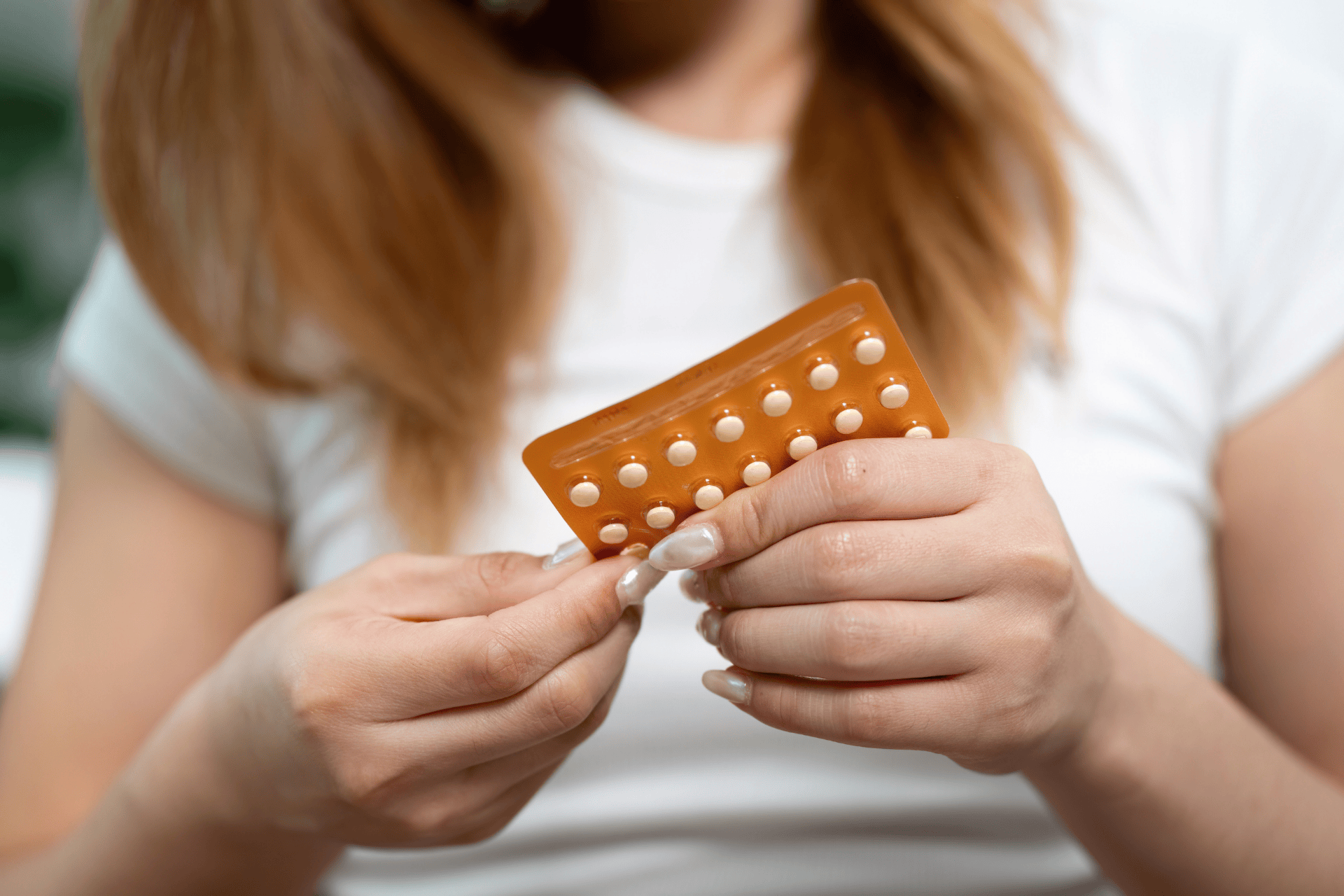 A person holding a blister pack of small, round oral contraceptive pills