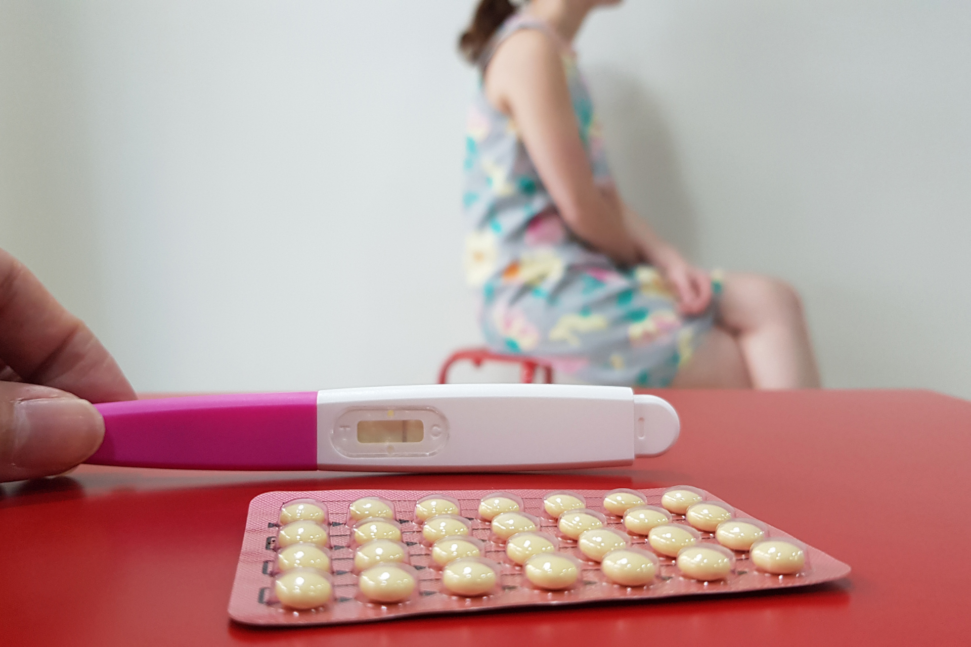 Pregnancy test and birth control pills on a table with a woman sitting blurred in the background
