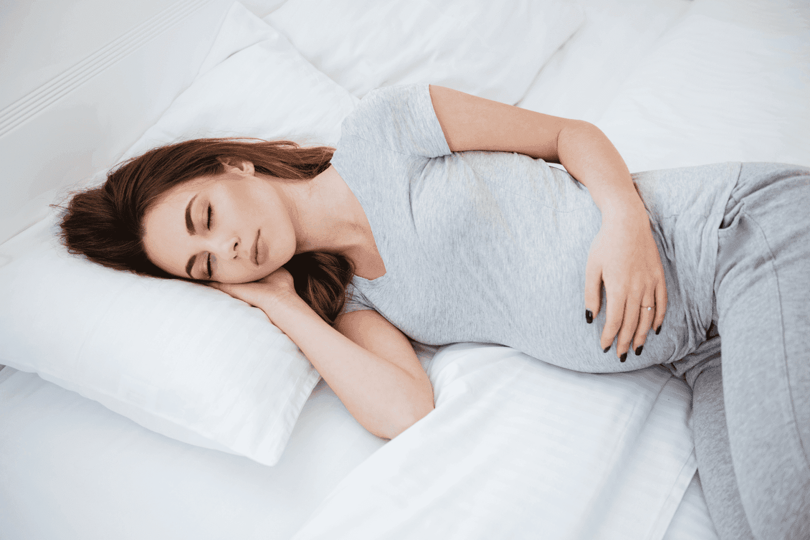 Pregnant woman lying on her side in bed, wearing a grey outfit, sleeping