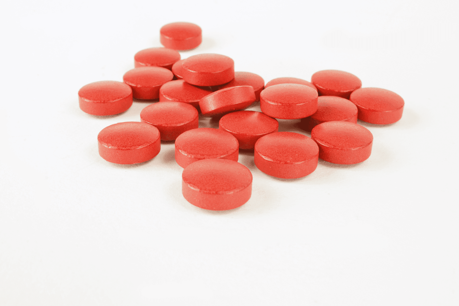 Red tablets scattered on a white surface.
