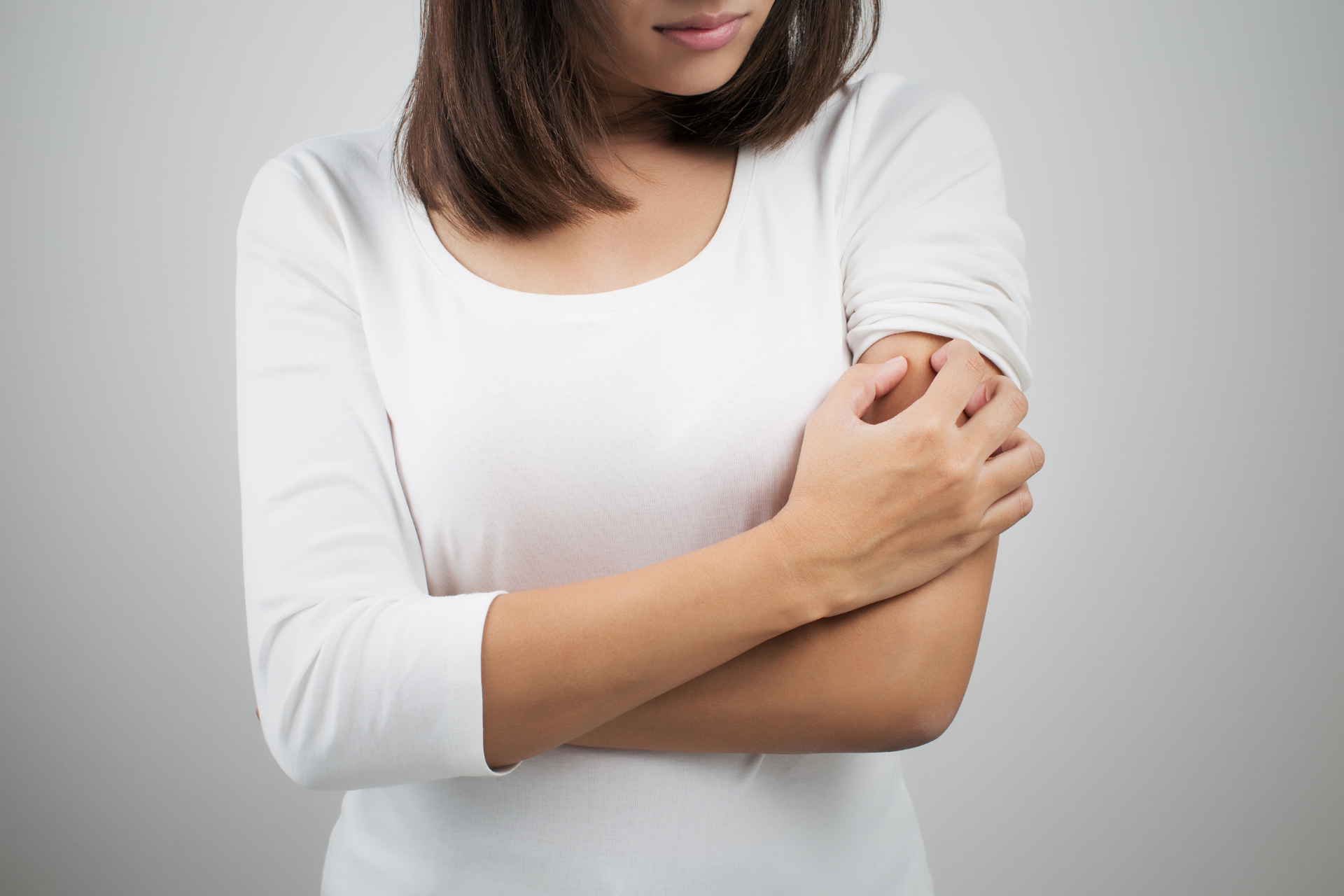 A person clutching their upper arm with a pained expression, appearing to have discomfort or itchiness