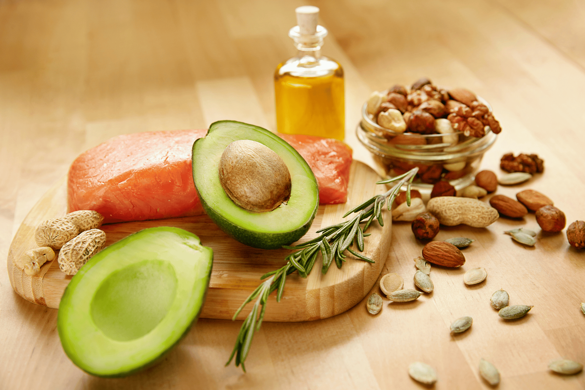 Selection of healthy fats including avocado, salmon, nuts, seeds, and olive oil arranged on a wooden surface