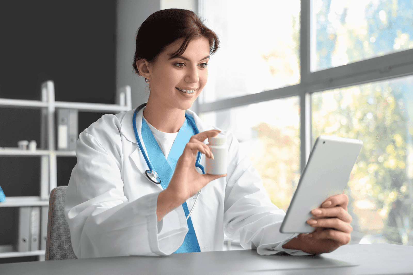 Smiling doctor holding a pill bottle while conducting an online consultation on a tablet.