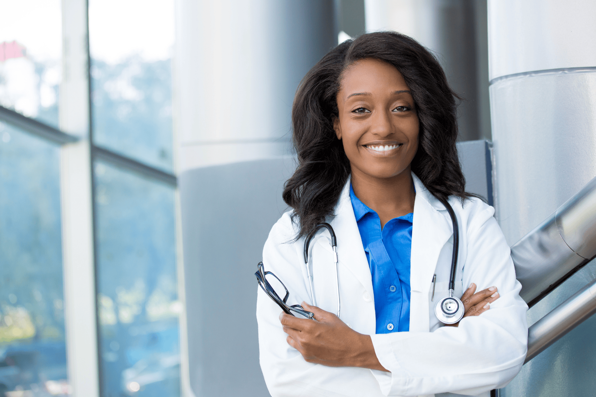 Smiling doctor with a stethoscope standing confidently in a modern medical building.