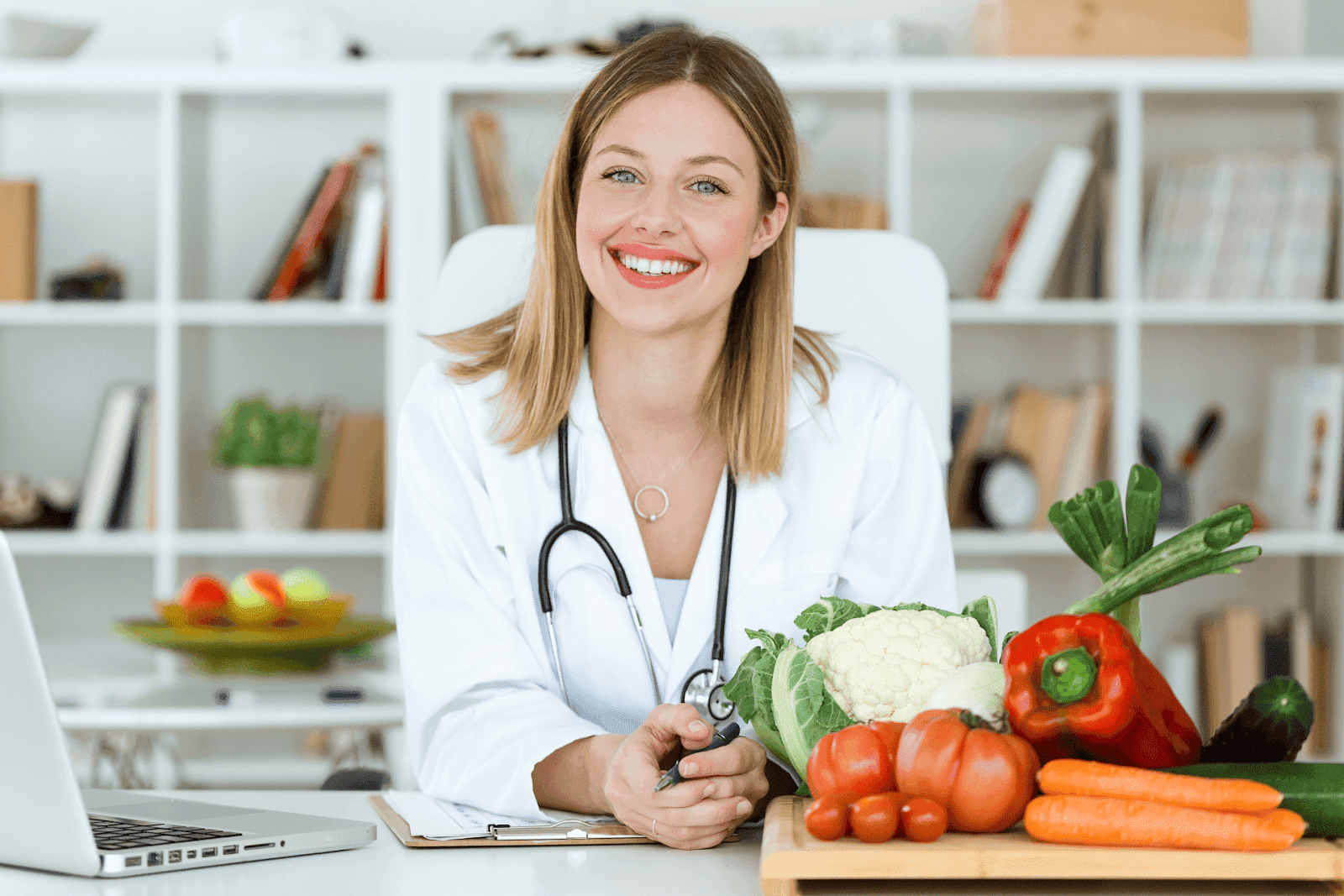 Smiling female doctor with a stethoscope sitting at a desk with fresh vegetables