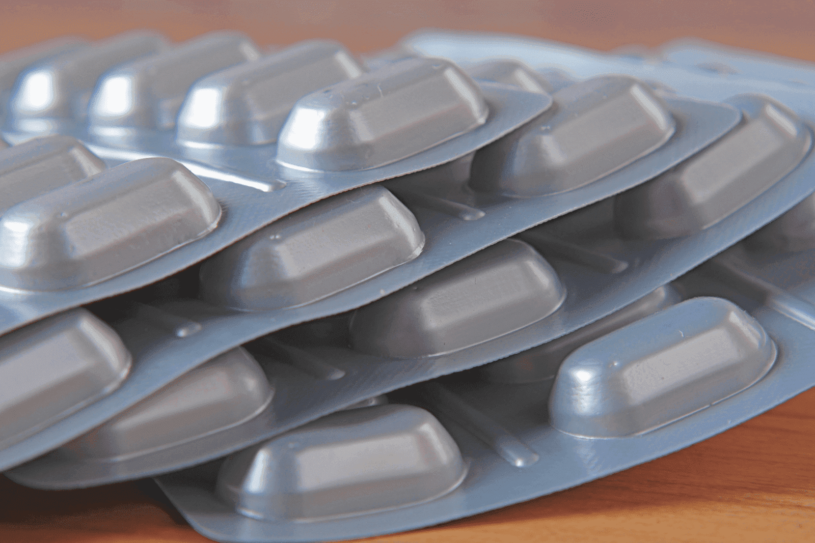 Stacked blister packs of medication on a wooden surface.