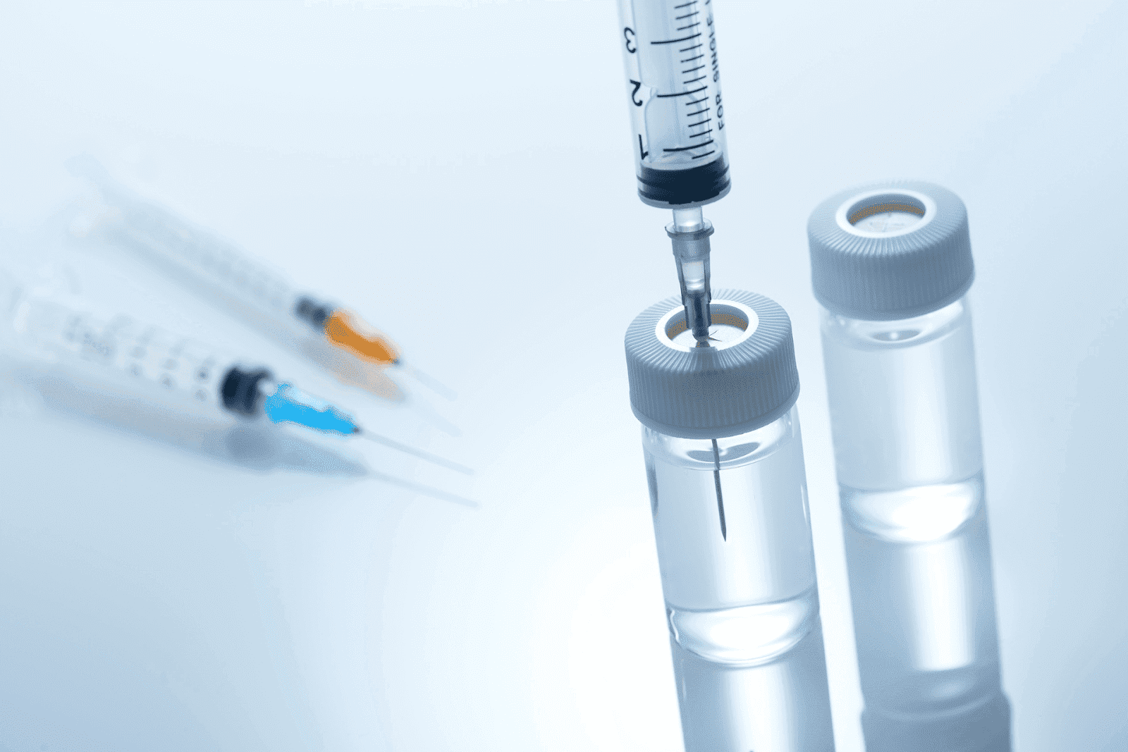 Syringe inserted into a vial with other syringes and bottles in the background