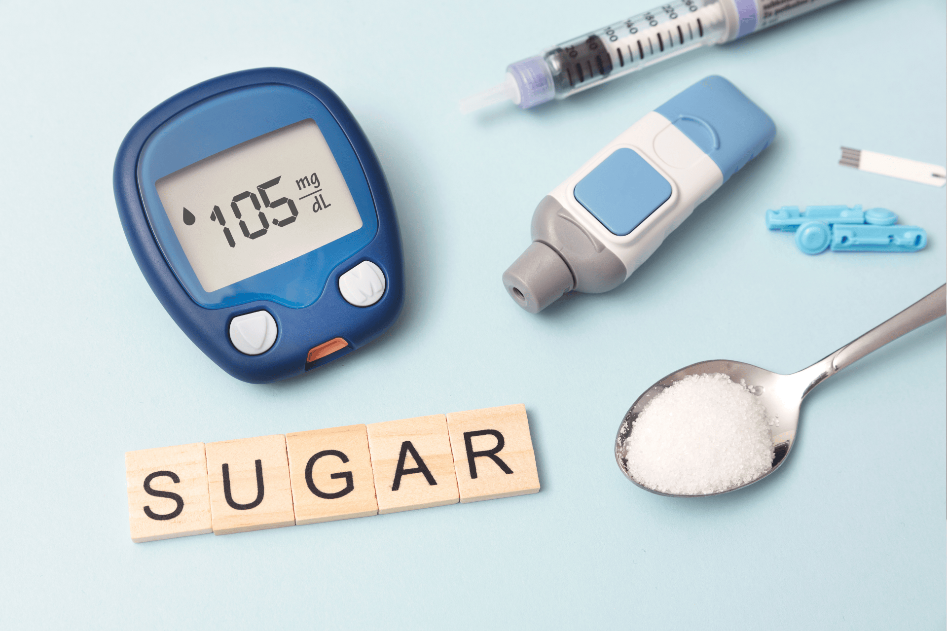 Diabetes testing tools, syringe, and a spoonful of sugar with the word ‘SUGAR’ spelled out.