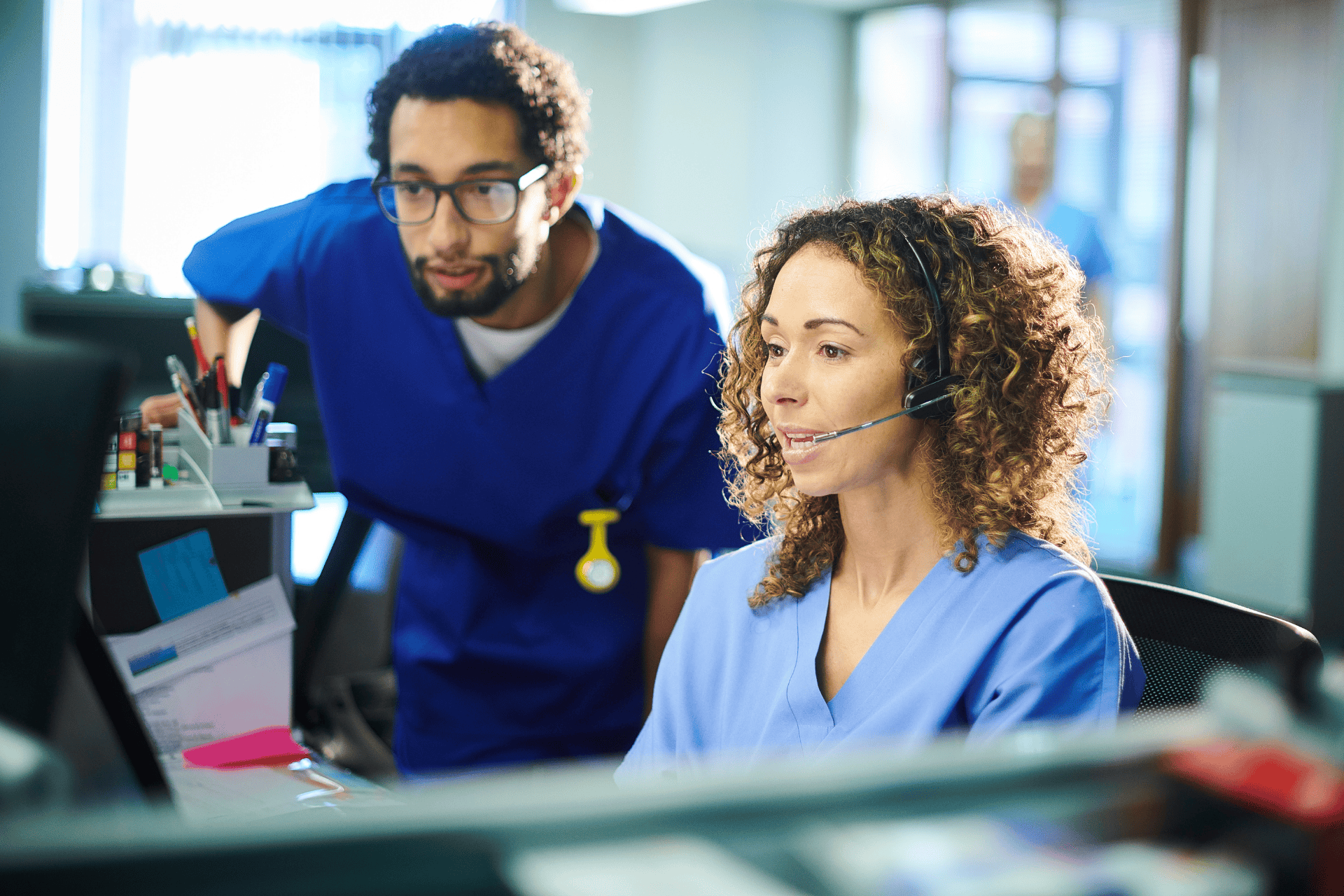 Two healthcare professionals in scrubs working together at a computer station.
