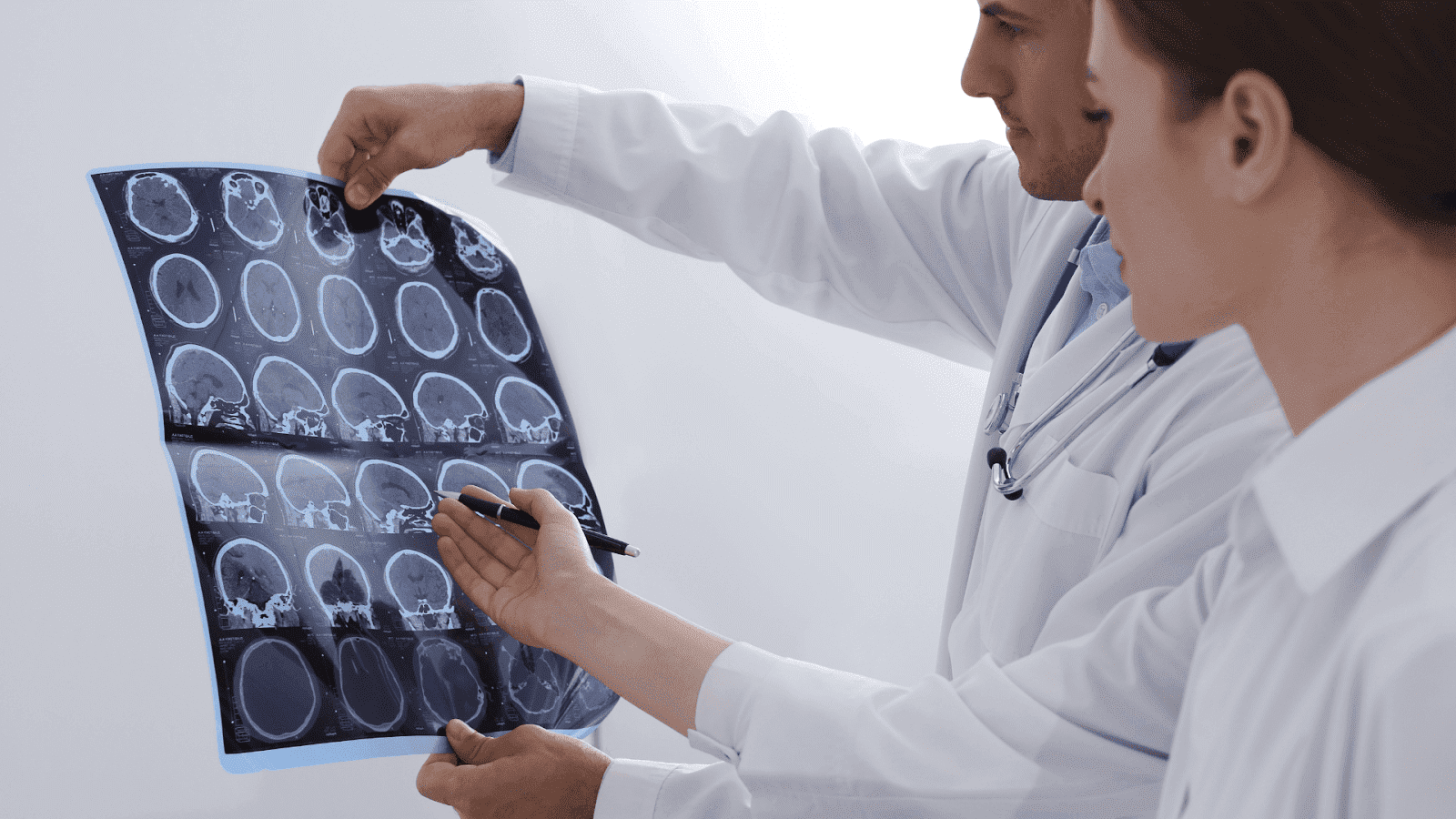 Two medical professionals examine a series of brain CT or MRI scans together, discussing a diagnosis.
