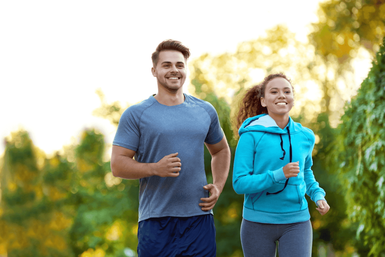 Two people jogging together outdoors on a tree-lined path.