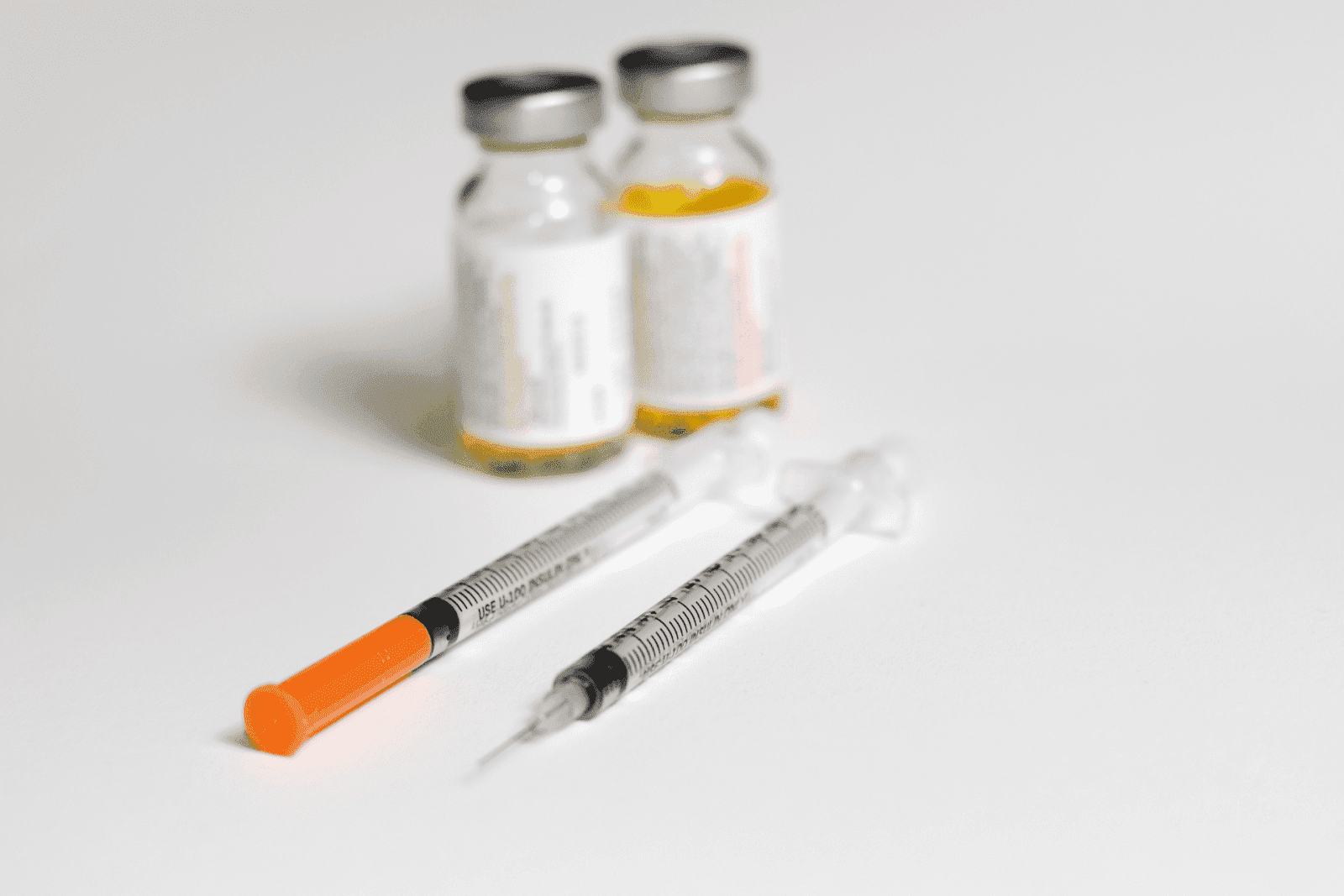 Two syringes and medicine vials with yellow liquid on a white surface