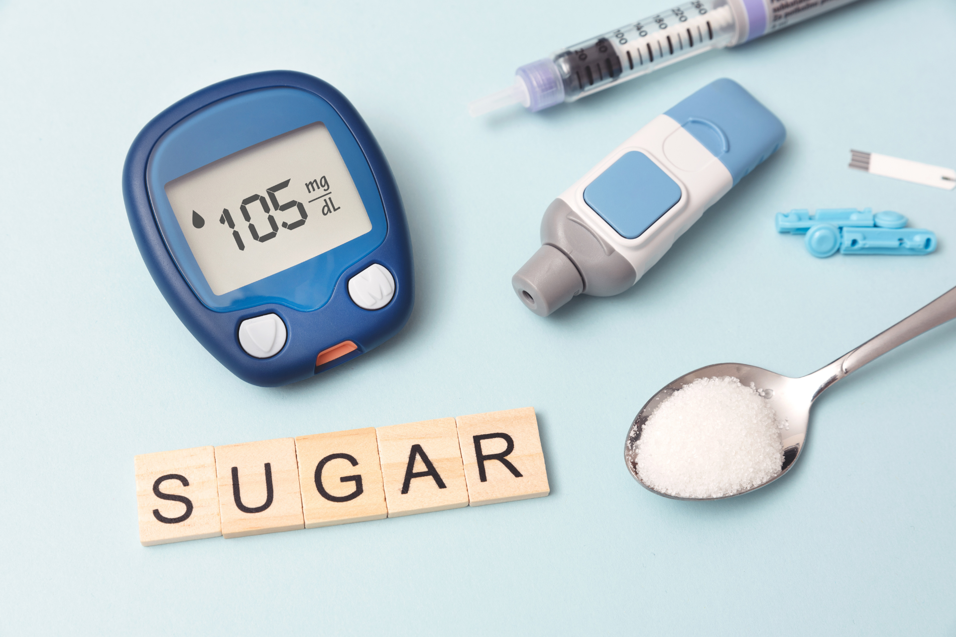 Diabetes testing supplies, including a glucose meter reading 105 mg/dL, a lancet device, a syringe, and a spoon of sugar