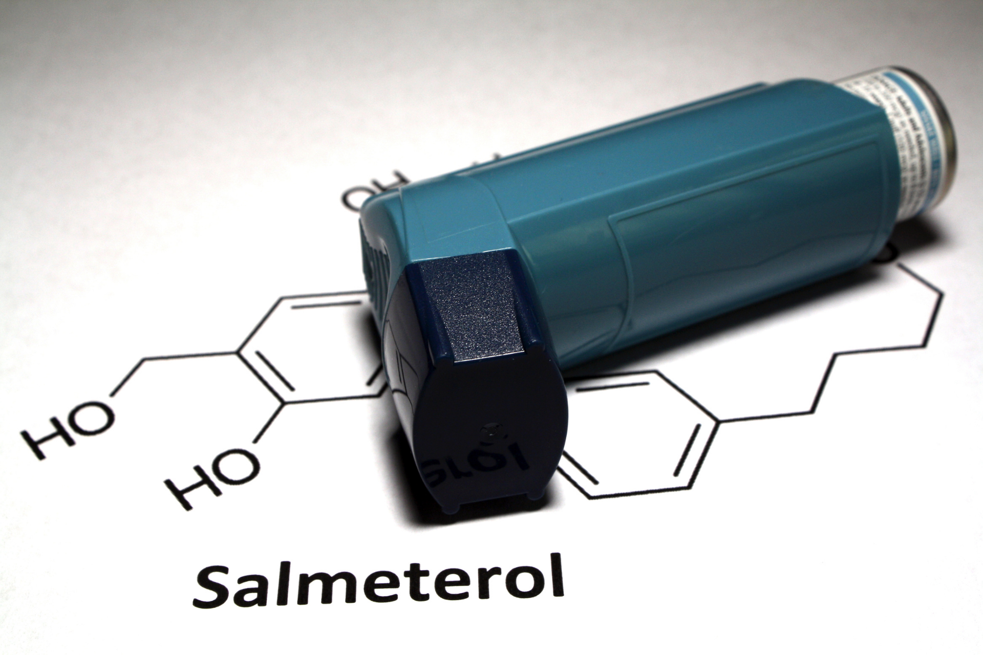 Blue asthma inhaler placed on top of a salmeterol chemical structure diagram