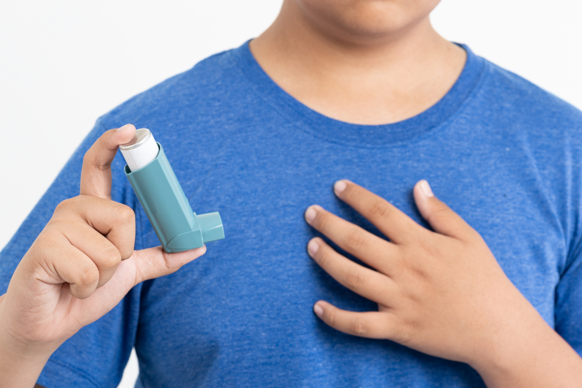 Child holding an asthma inhaler in one hand while placing the other hand on their chest