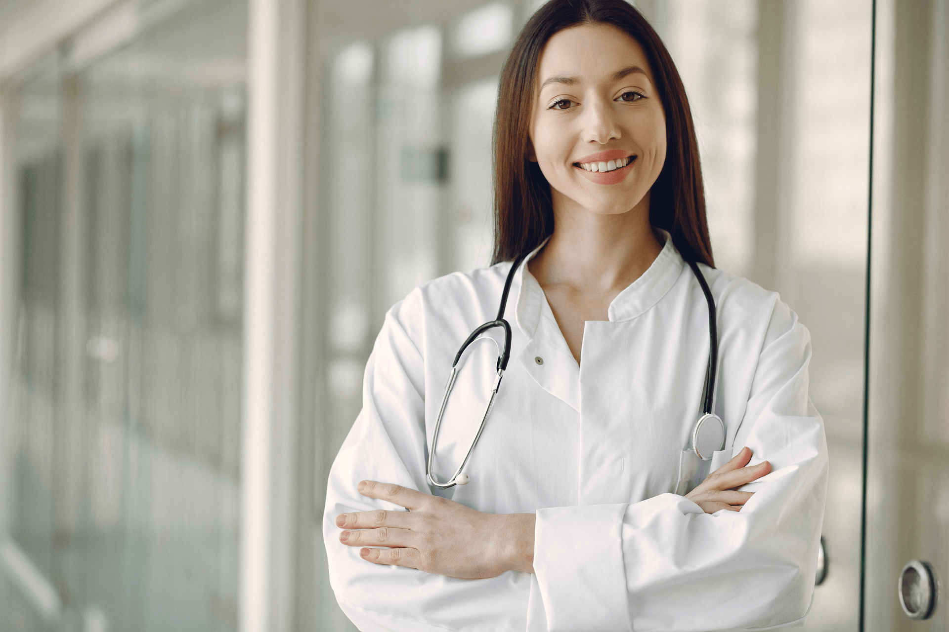 Female doctor smiling with arms crossed, wearing a white coat and stethoscope.