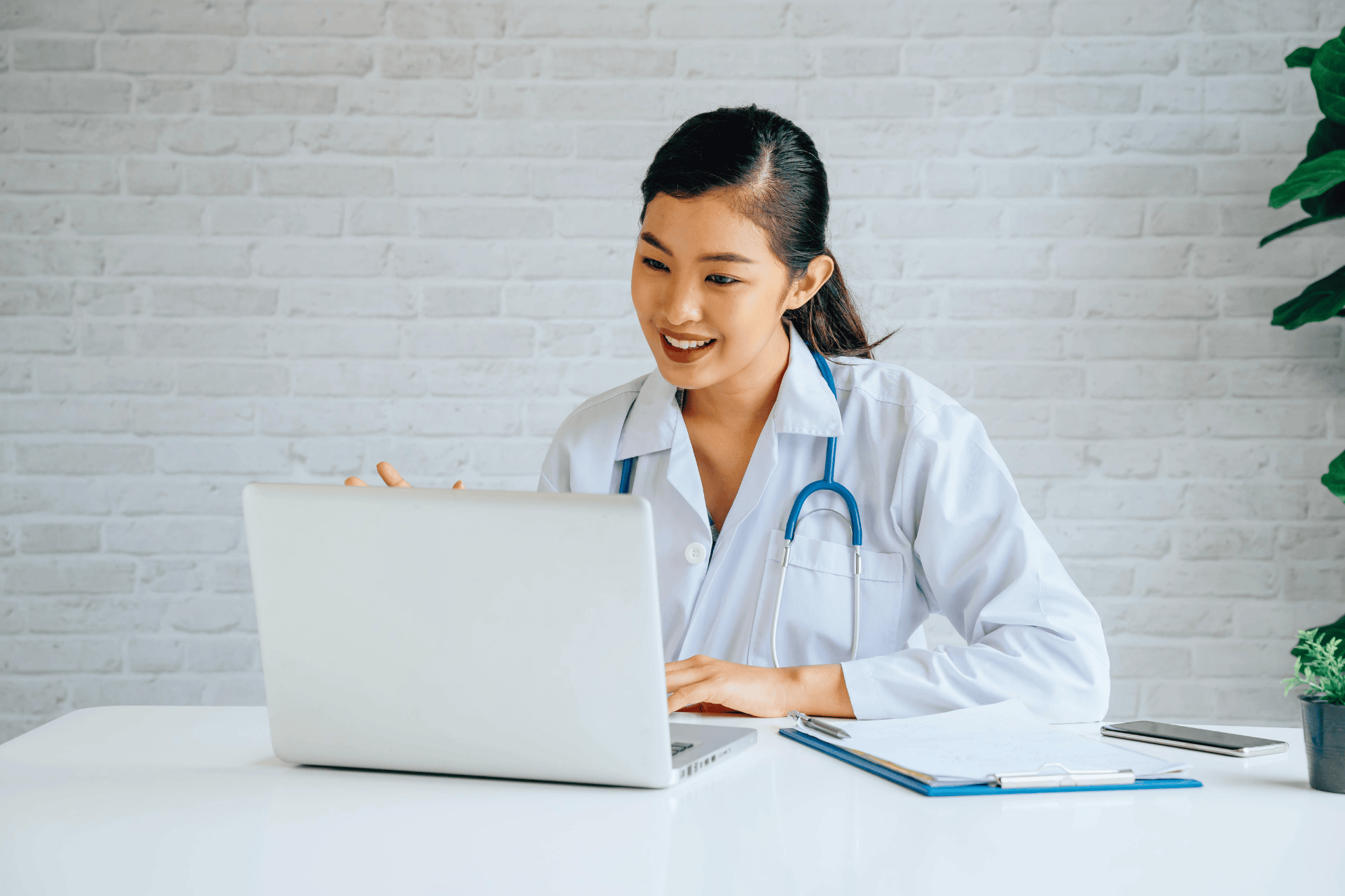 Smiling doctor with a stethoscope talking to a patient through a laptop.