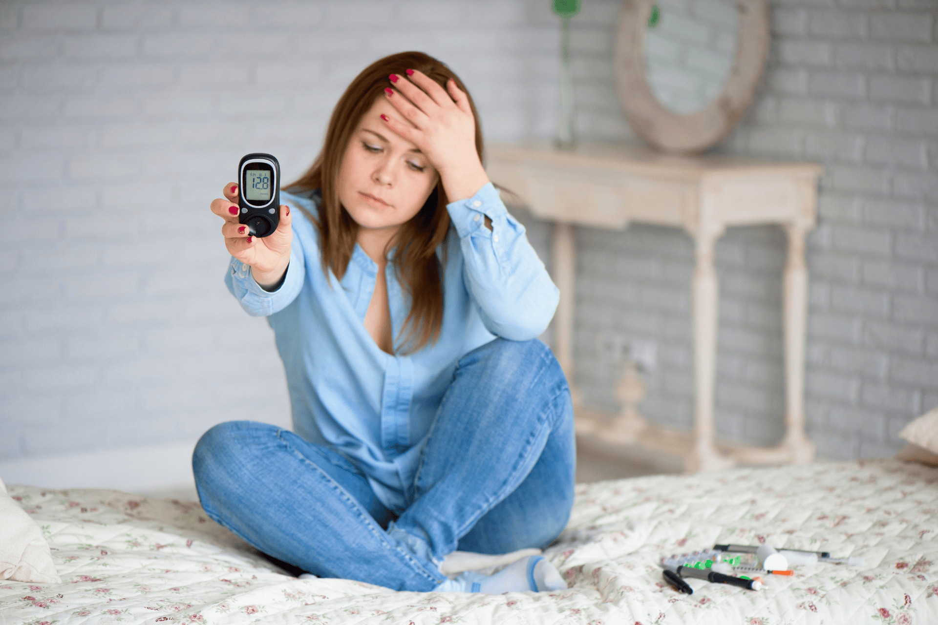 Woman sitting on a bed looking worried while showing a blood glucose meter.