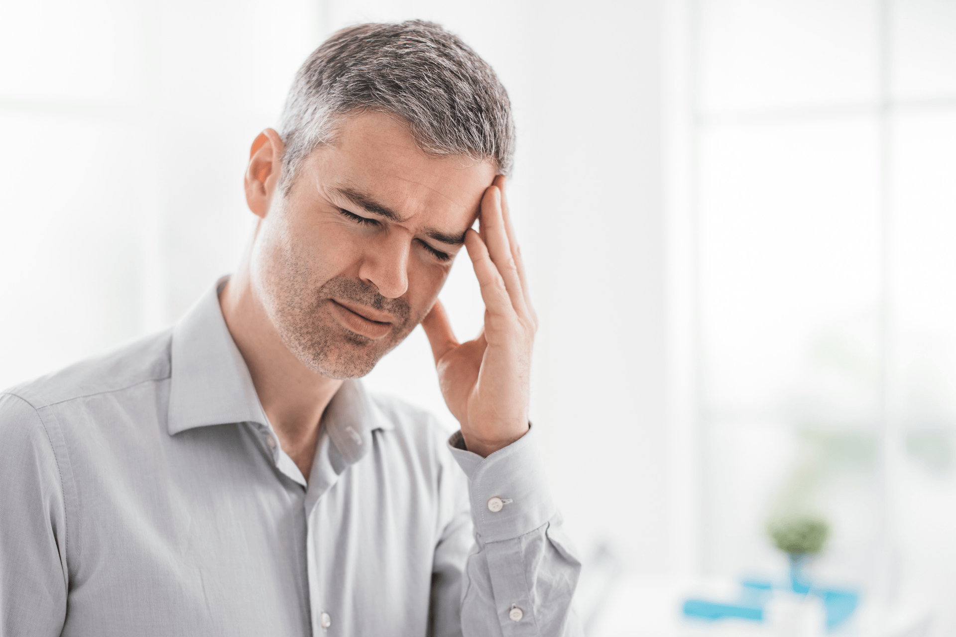 Man touching his head and wincing in pain, showing signs of a headache.