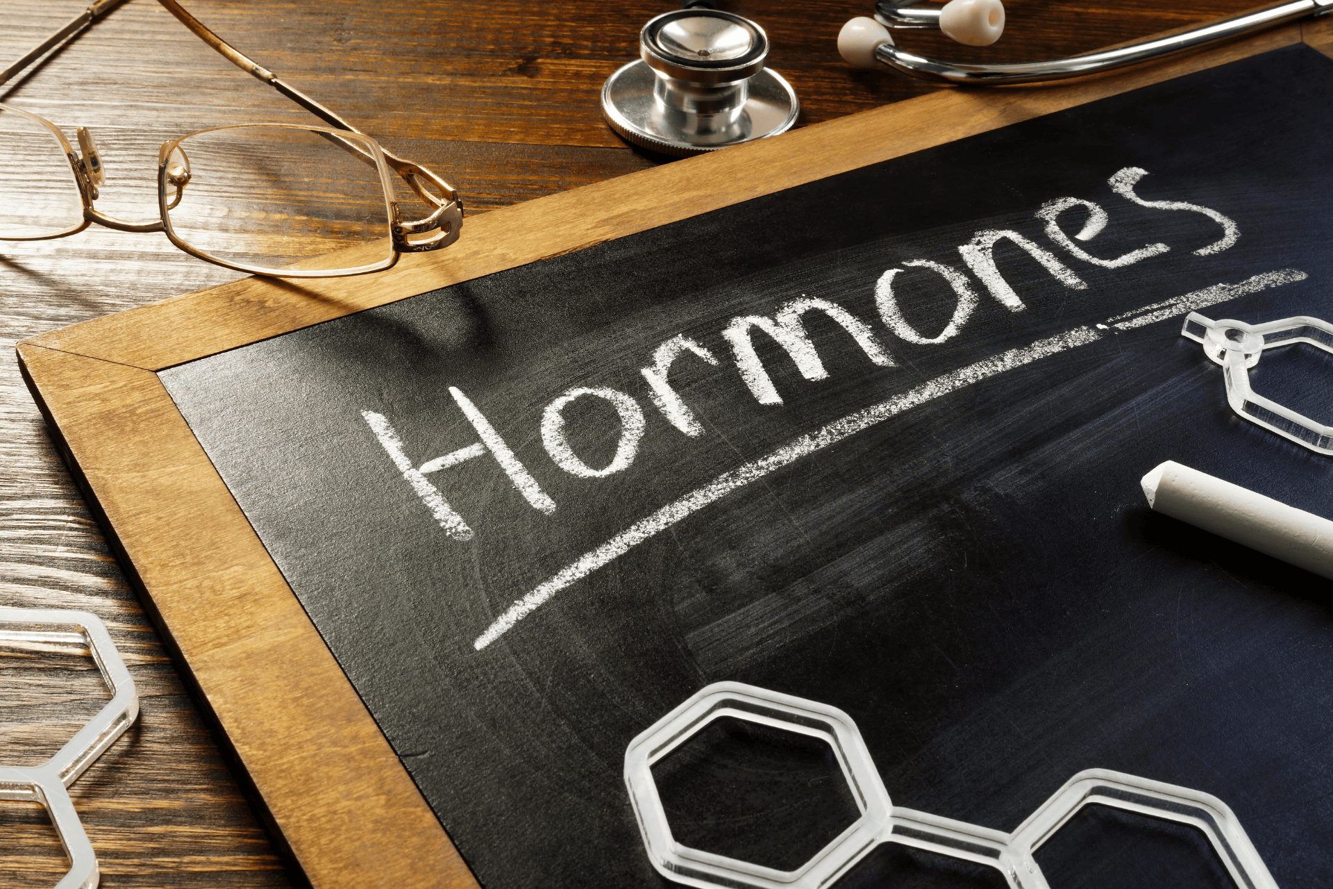 Chalkboard with the word ‘Hormones’ written on it beside a stethoscope and glasses.